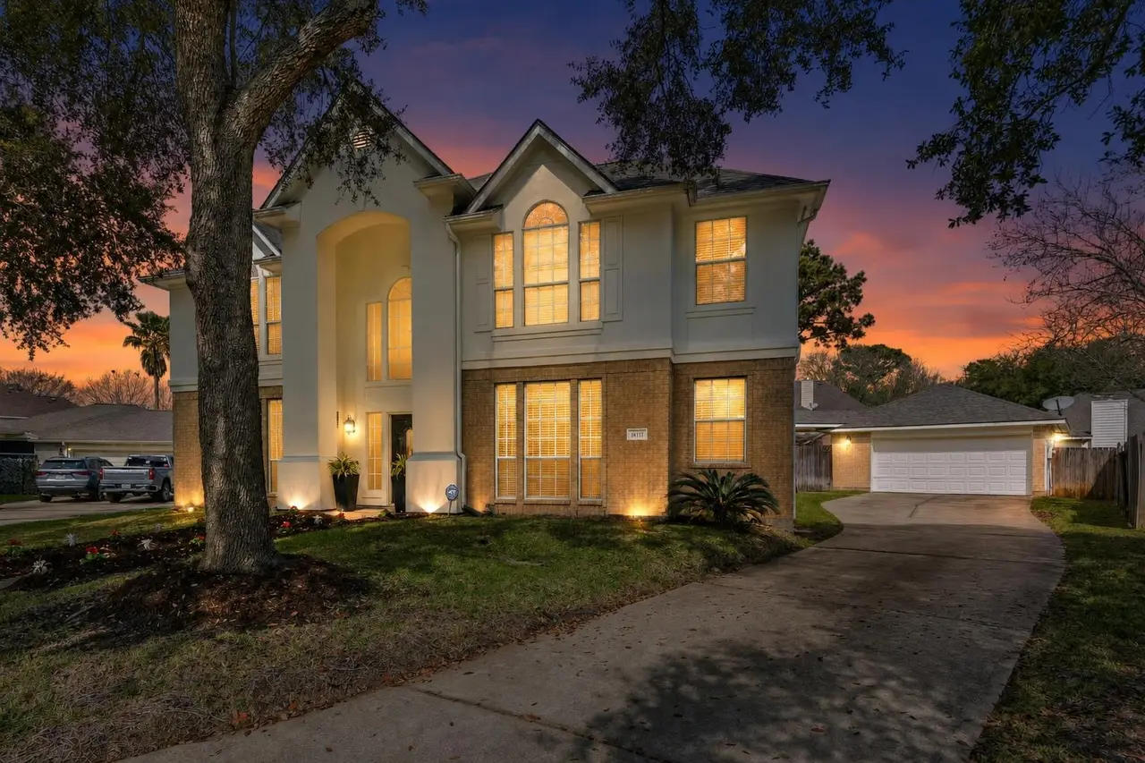 The same home at dusk, with a sunset sky, warm window glow, and lit landscaping