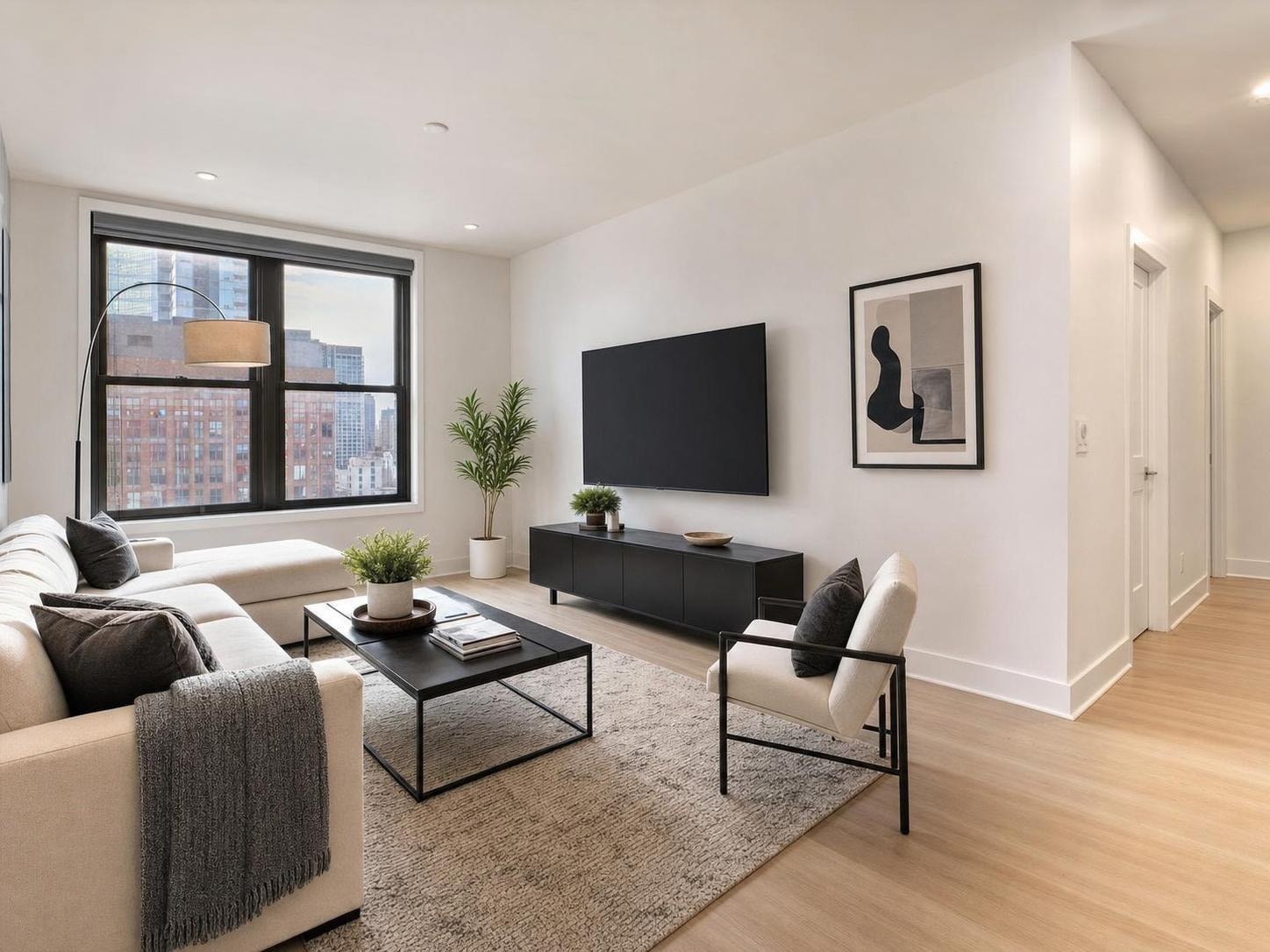 Modern living room with beige sectional, black metal coffee table, armchair, large window, and light wood floor.