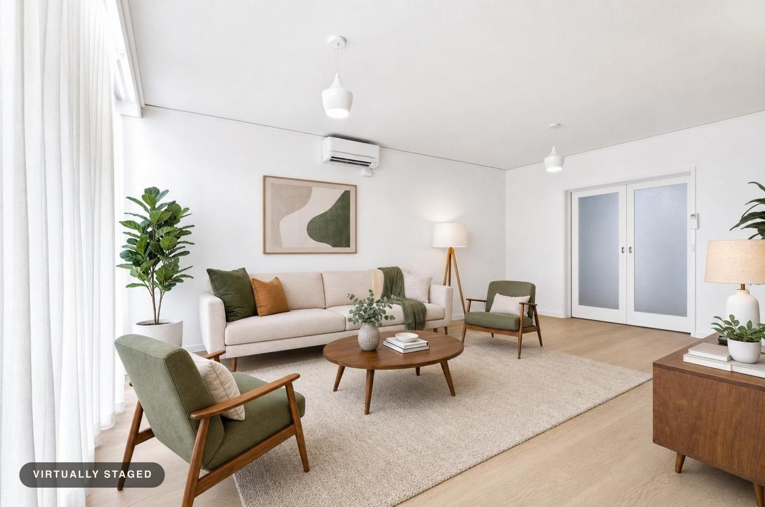 Living room with beige sofa, green armchairs, round wood coffee table, white walls, plants, and wood furniture on a light rug.