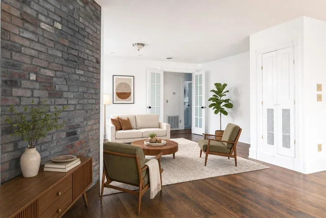 Living room with beige sofa, two olive Green armchairs, wooden coffee table, brick accent wall, and wooden sideboard.