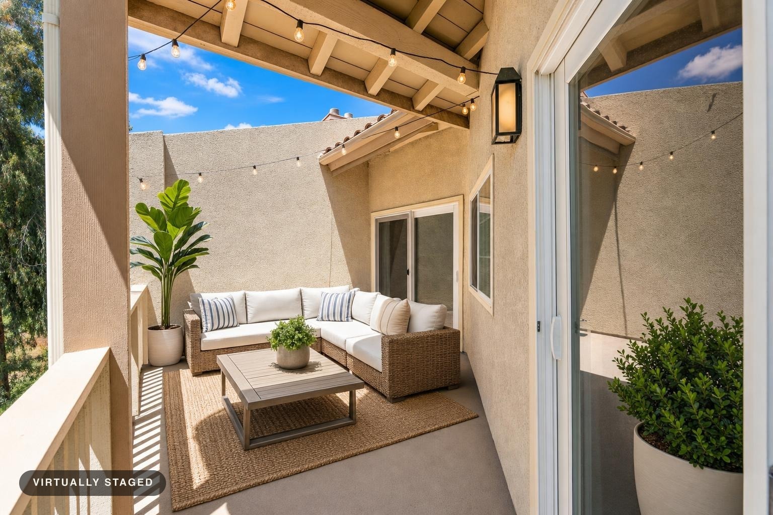 Backyard patio with L-shaped wicker sofa, coffee table on natural fiber rug, string lights above, and potted plants.