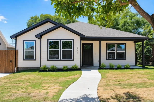 Modern single-story house with white siding and black trim, concrete walkway, and lawn under a tree.