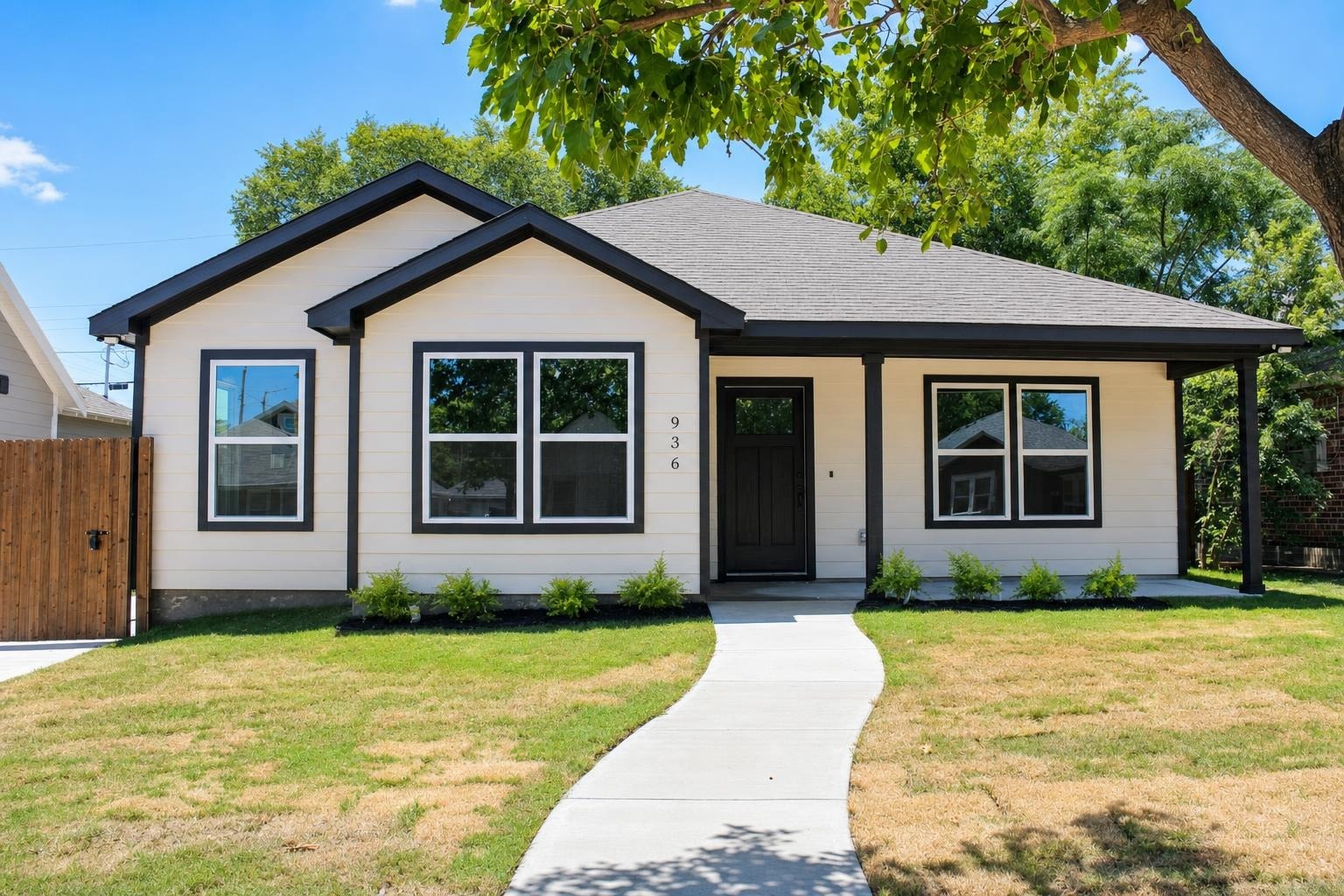 Modern single-story house with white siding and black trim, concrete walkway, and lawn under a tree.