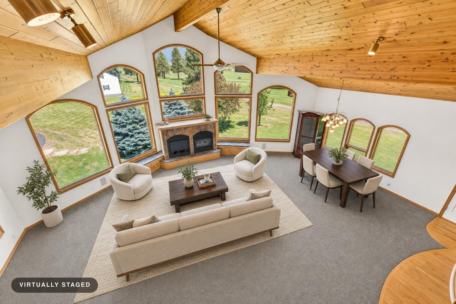 Living room with large arched windows, vaulted wood-paneled ceiling, beige sofa and chairs, dark wood coffee table, and dining table with cream chairs.