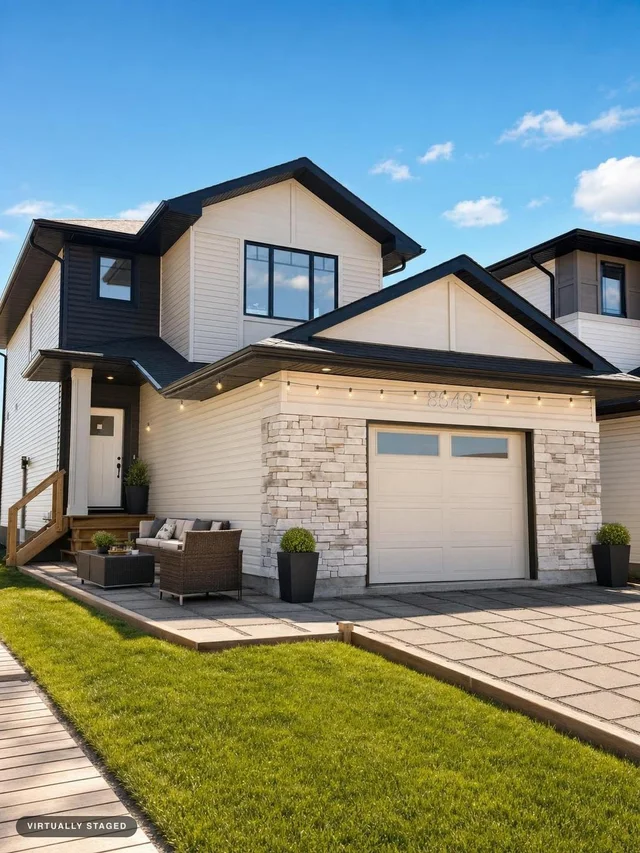 Modern two-story house with beige siding, stone accents, black-trimmed large windows, and a small outdoor patio set with greenery.