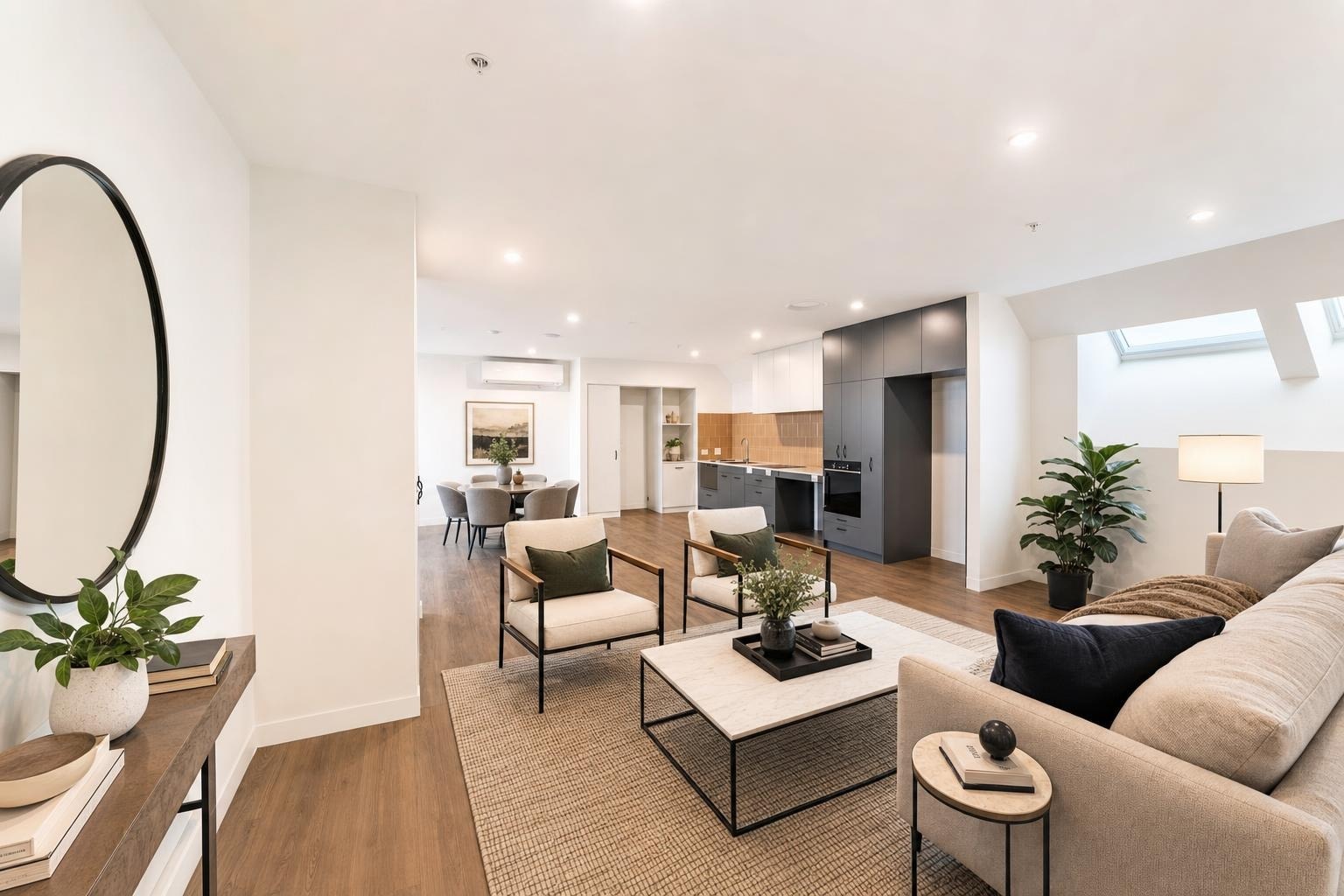 Open modern living room with beige sofa, two armchairs, coffee table, side table, floor lamp, and indoor plants.