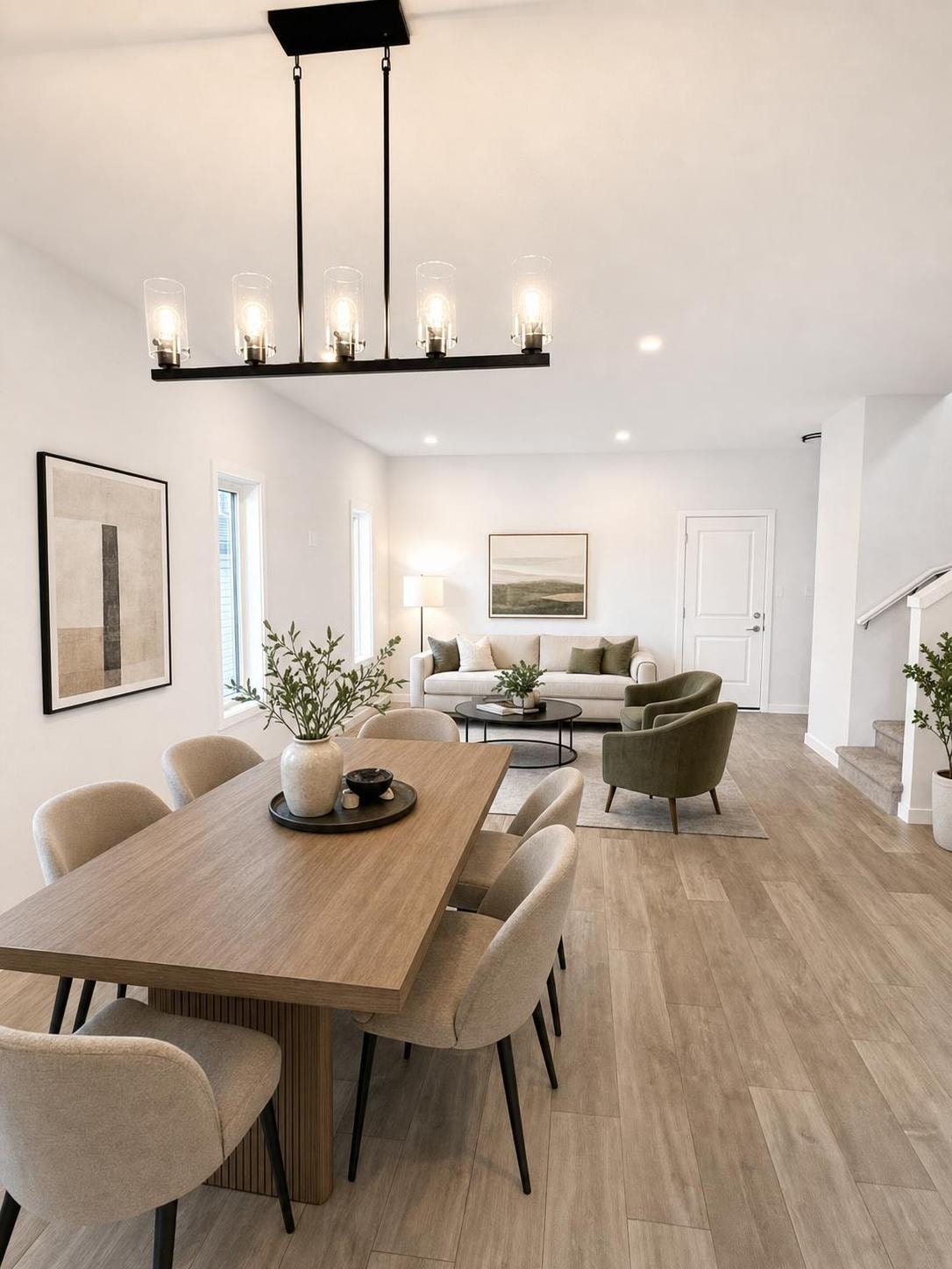 Modern living and dining space with a wooden table, beige chairs, gray sofa, green armchairs, and black hanging light fixture.