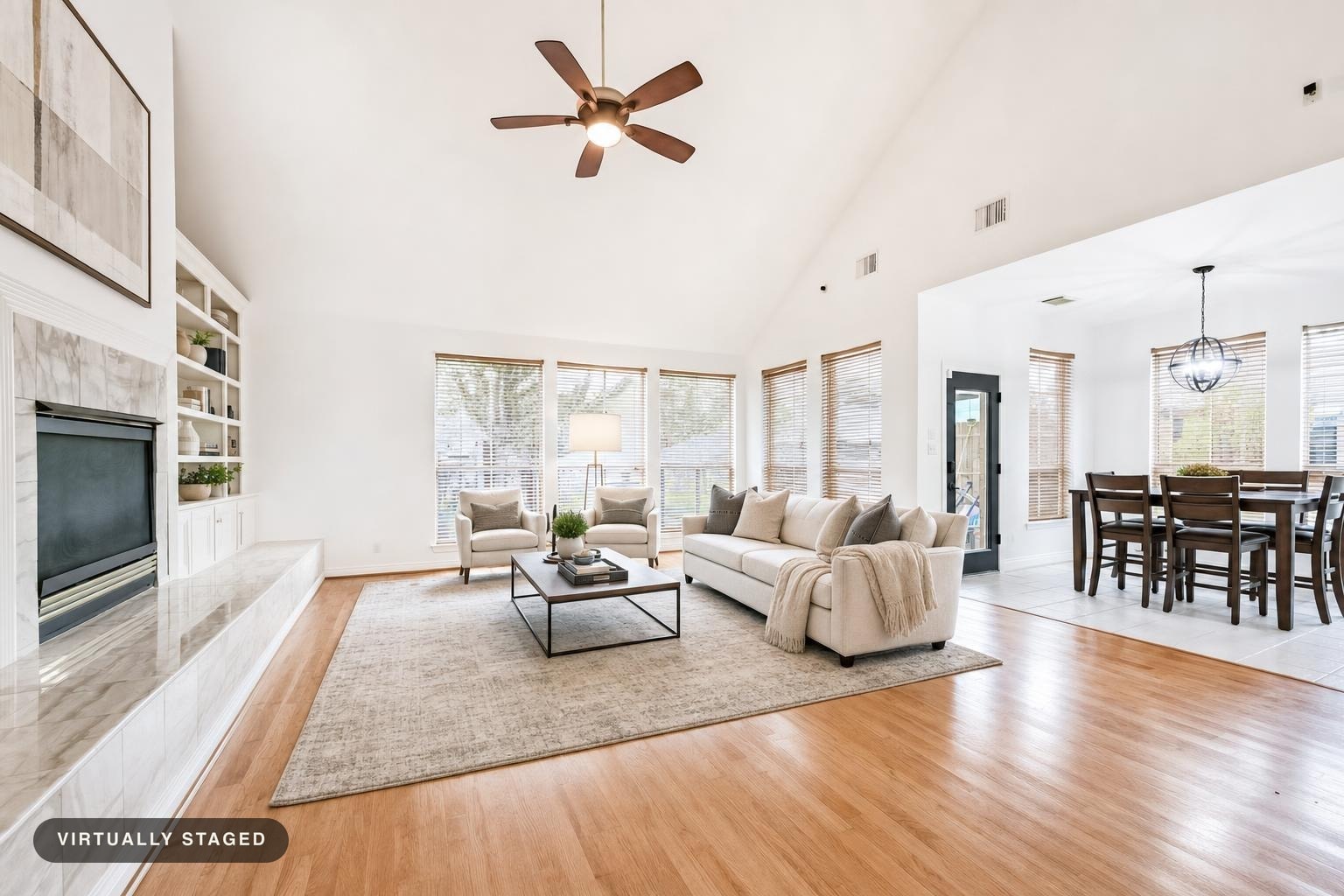 Bright living room with vaulted ceilings, large windows, light sofa, two armchairs, rectangular coffee table, and a fireplace.