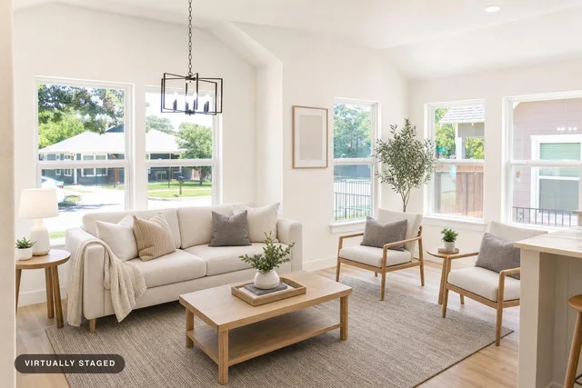 Scandinavian living room with beige sofa, two light wood armchairs, wooden coffee table, area rug, and large windows.