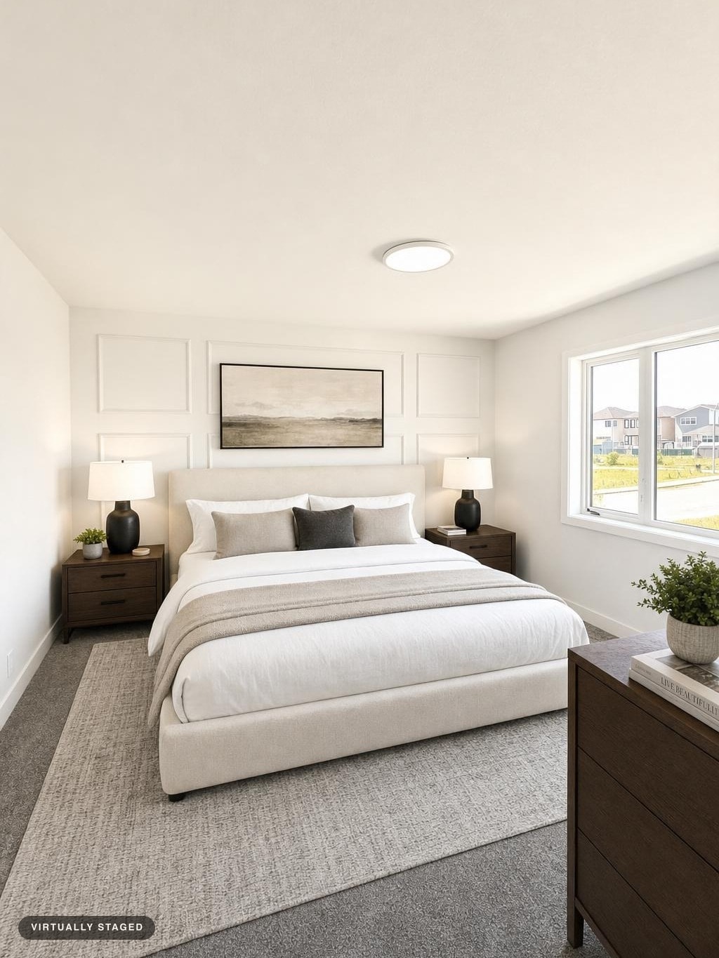 Modern bedroom with beige upholstered bed, white and gray bedding, dark wood nightstands with black lamps, and a large window.