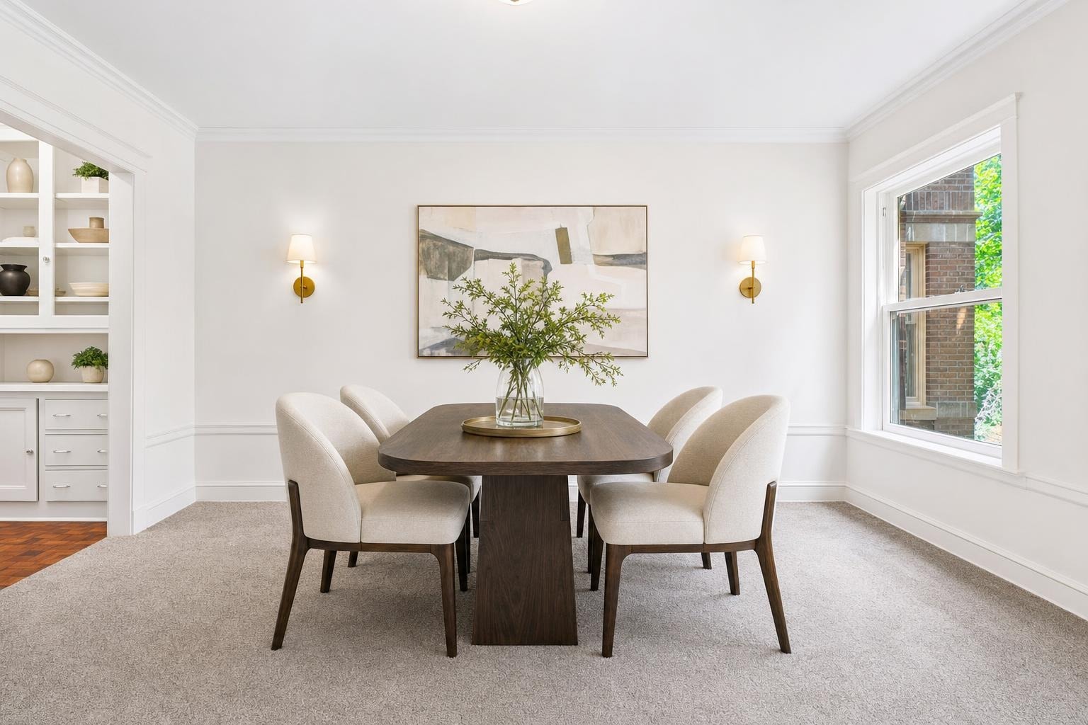 Modern dining room with a dark wood rectangular table, six beige upholstered chairs, two gold wall sconces, and abstract paintings on white walls.