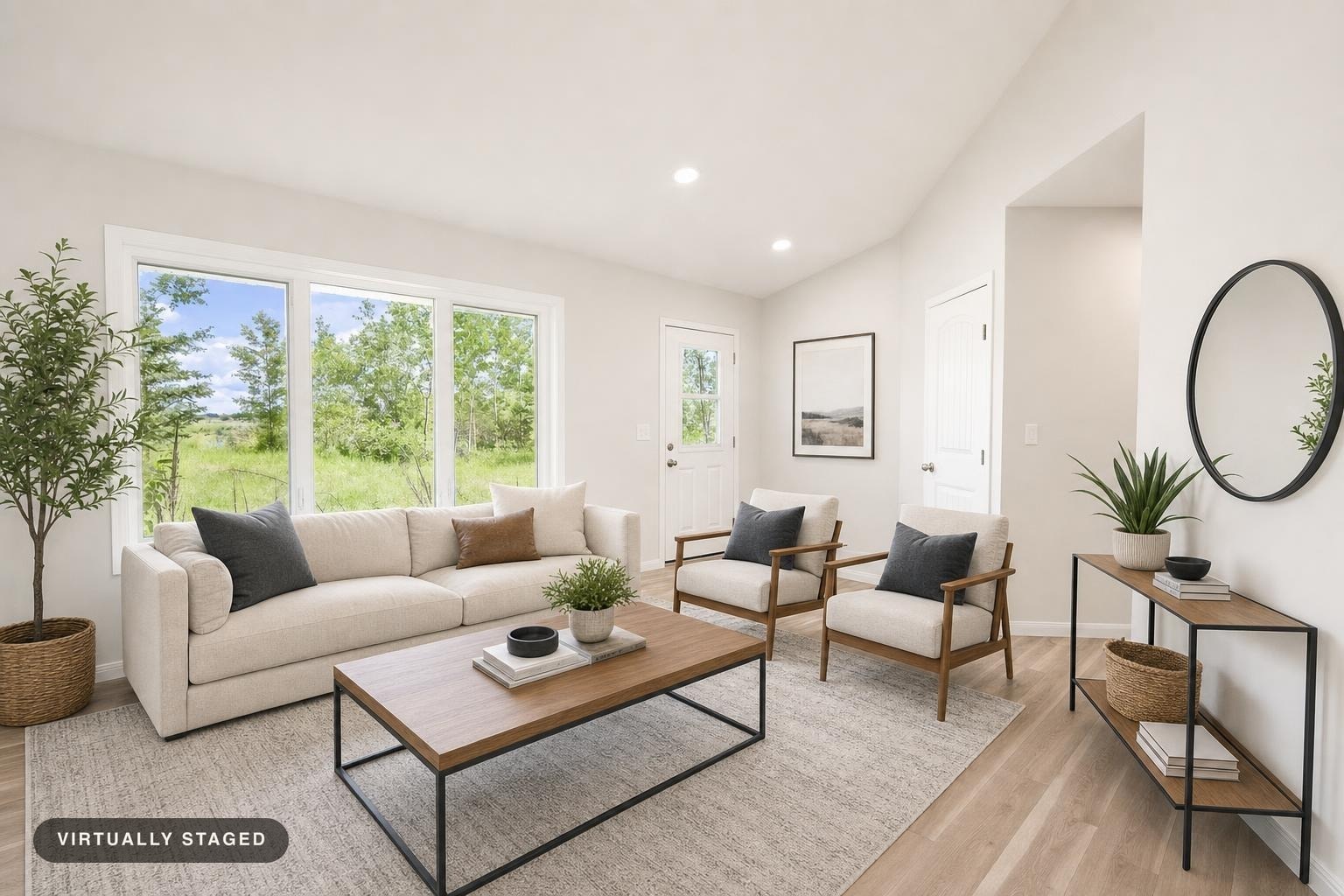 Modern living room with cream sofa, two armchairs, wood and metal coffee table, console table, plants, and large windows showing greenery.
