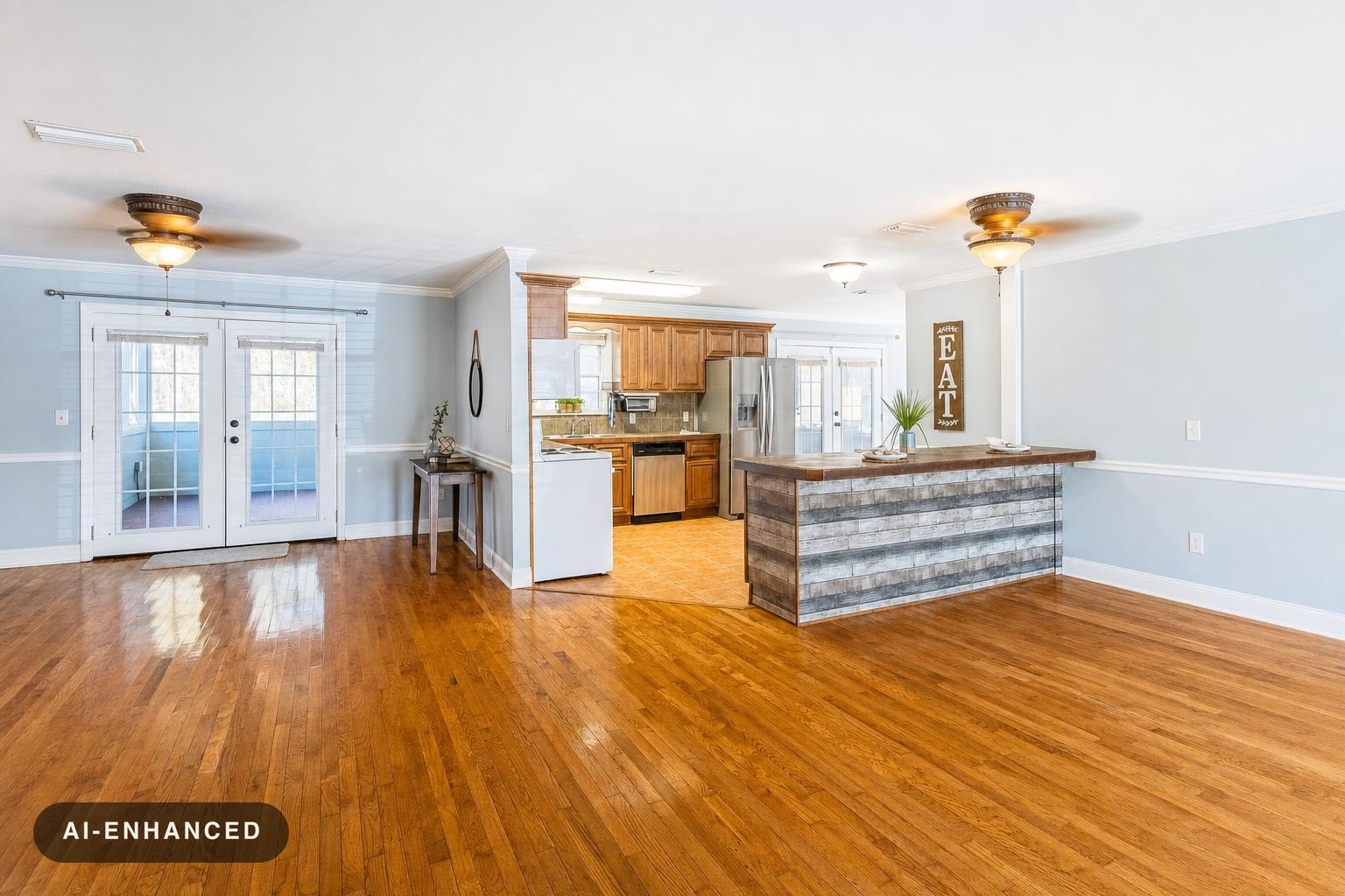 Open modern kitchen with wooden cabinets, stainless steel refrigerator, and a rustic island bar with 'EAT' sign on the wall.