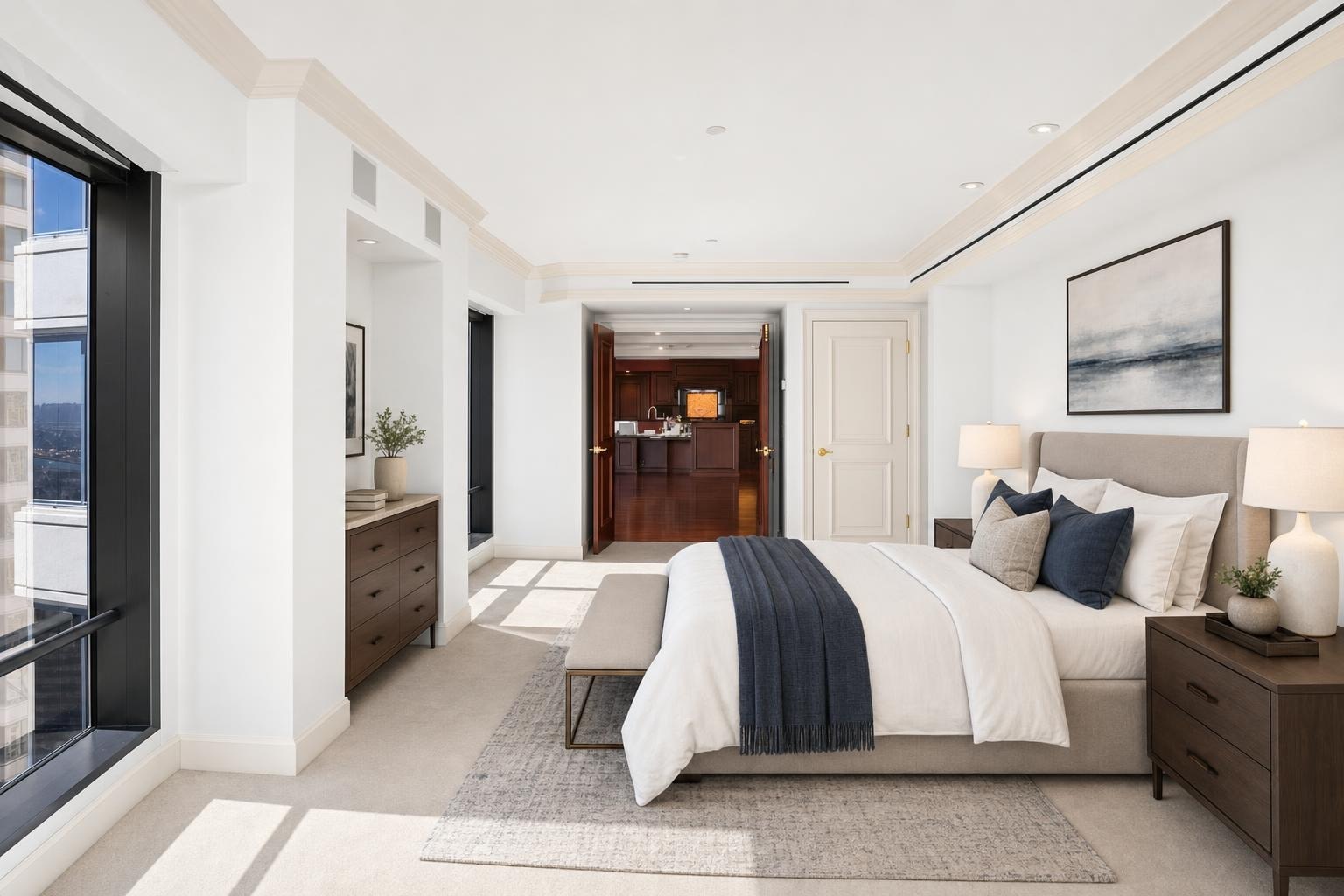 Modern luxury bedroom with beige upholstered bed, dark wood nightstands, navy accents, and large windows letting in natural light.