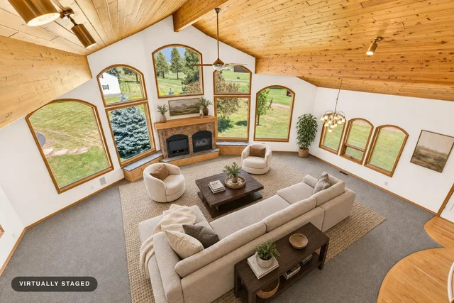 Living room with vaulted wood-paneled ceiling, large arched windows, beige sectional sofa, two round swivel chairs, and dark wood furniture.