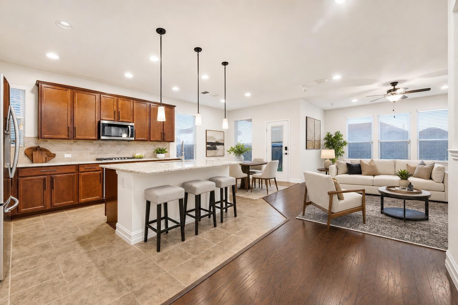 Open kitchen with warm wood cabinets and island with three stools, flowing into a light beige sectional and armchair living area.