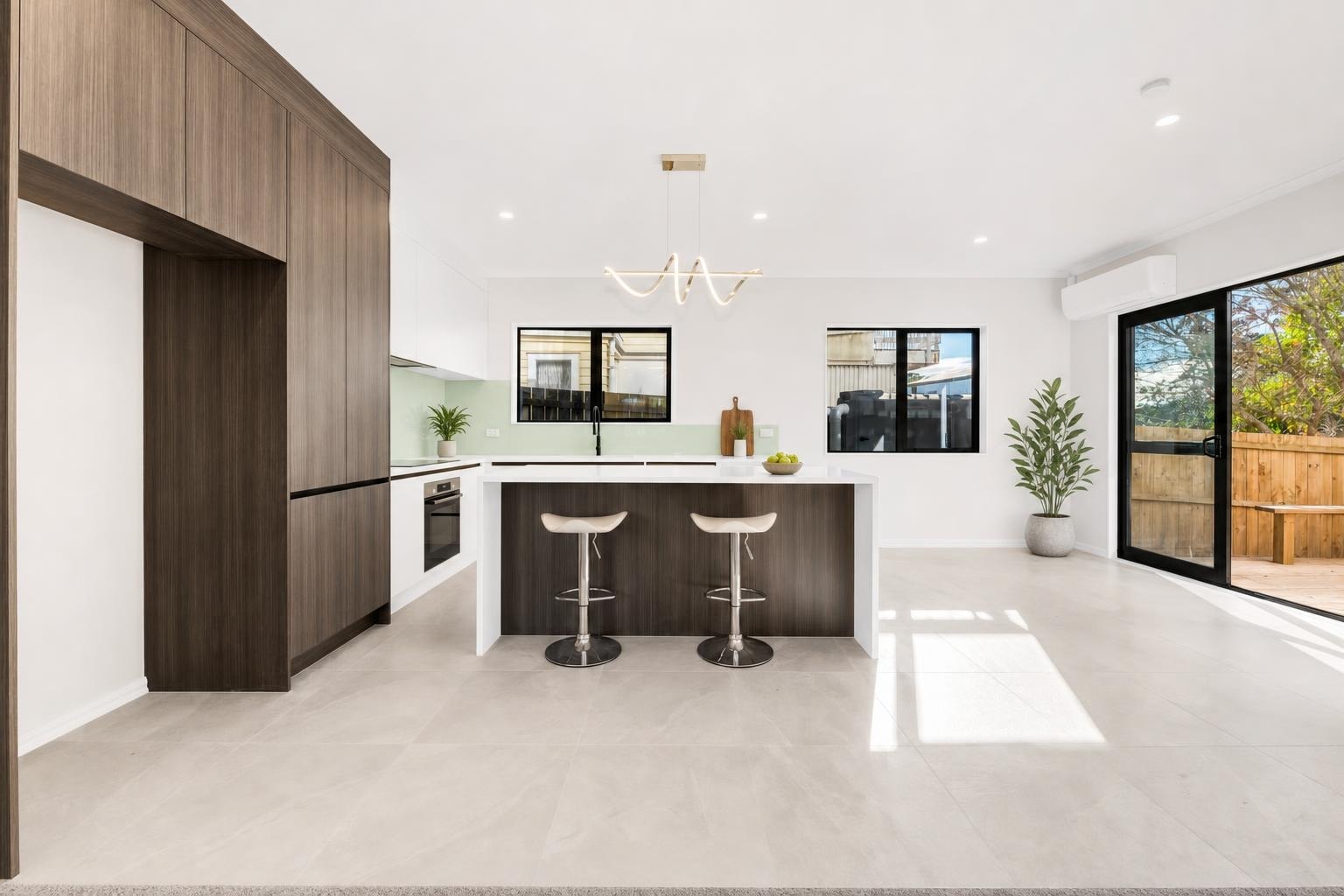 Modern kitchen with dark wood cabinets, white island, two bar stools, large windows, and sliding glass door to backyard.