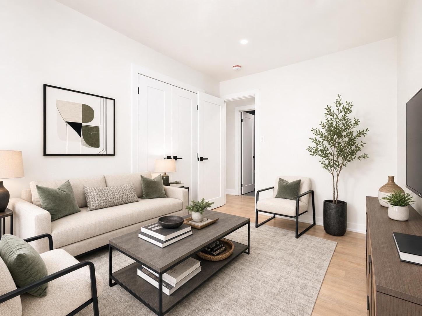 Modern living room with beige sofa and chairs, black metal accents, green pillows, coffee table, floor plant, and minimalist art.