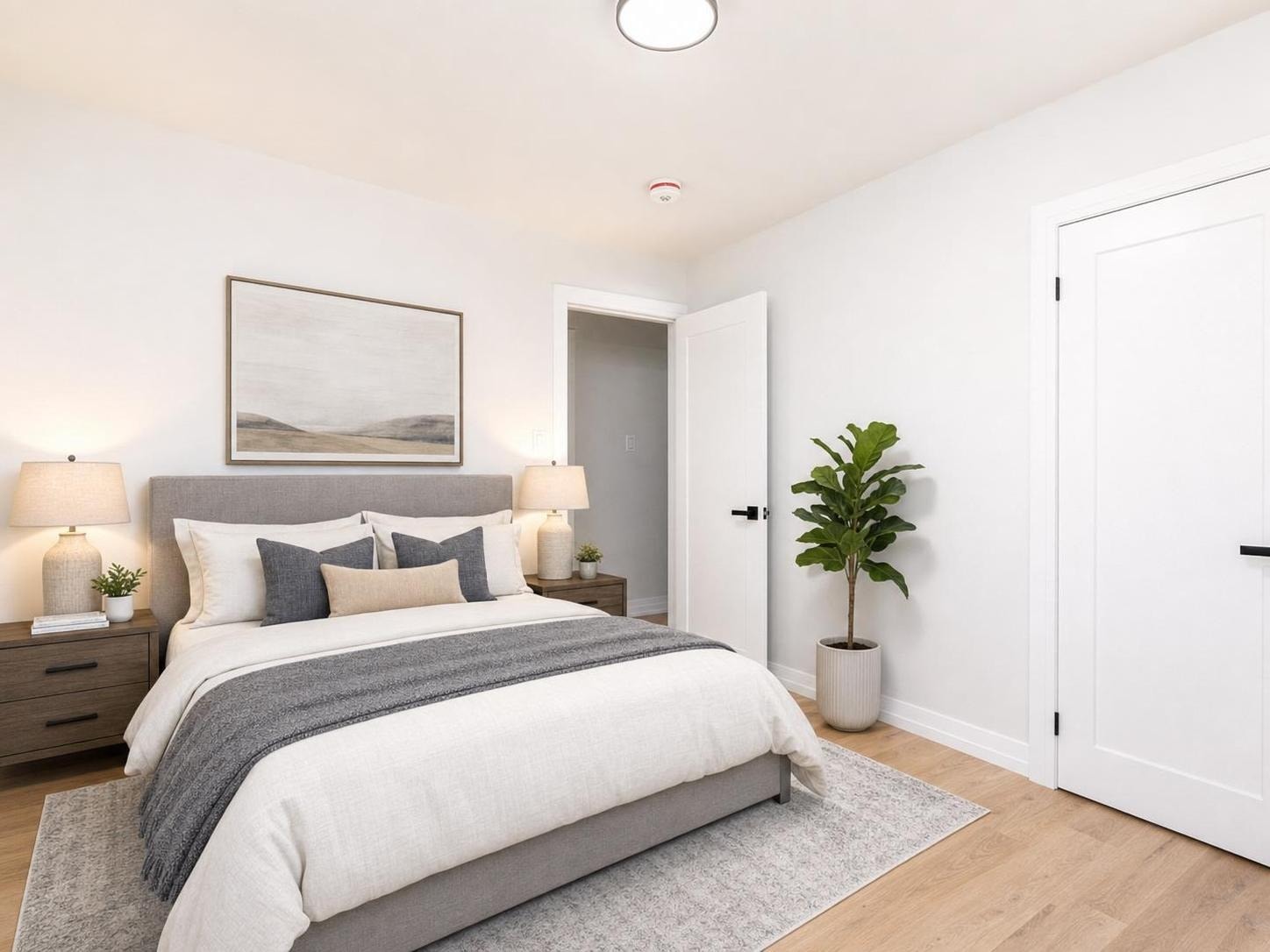 Modern bedroom with a gray upholstered bed, wooden nightstands with lamps, decorative pillows, light wood floor, and a potted green plant.