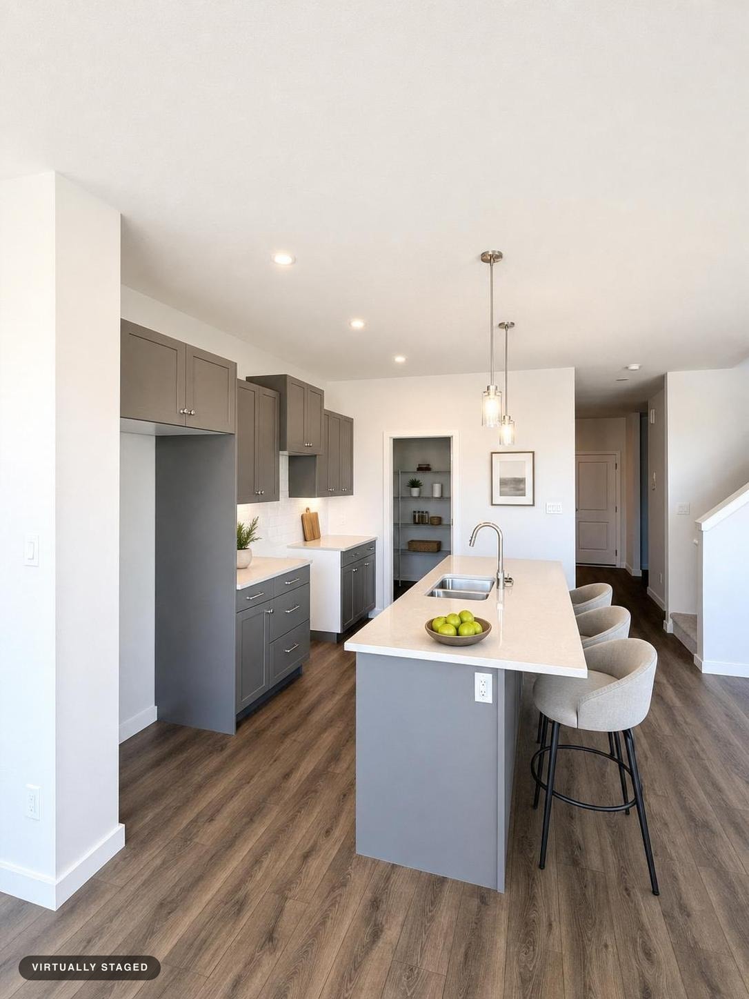 Modern kitchen with gray and white cabinetry, a white island with a sink, three beige bar stools, and wood-look flooring.