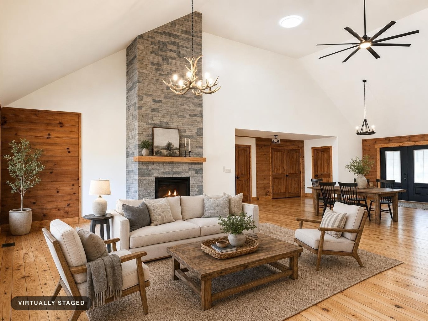 Living room with beige sofa and chairs, wooden coffee table on a rug, stone fireplace, and wooden flooring under vaulted ceiling.