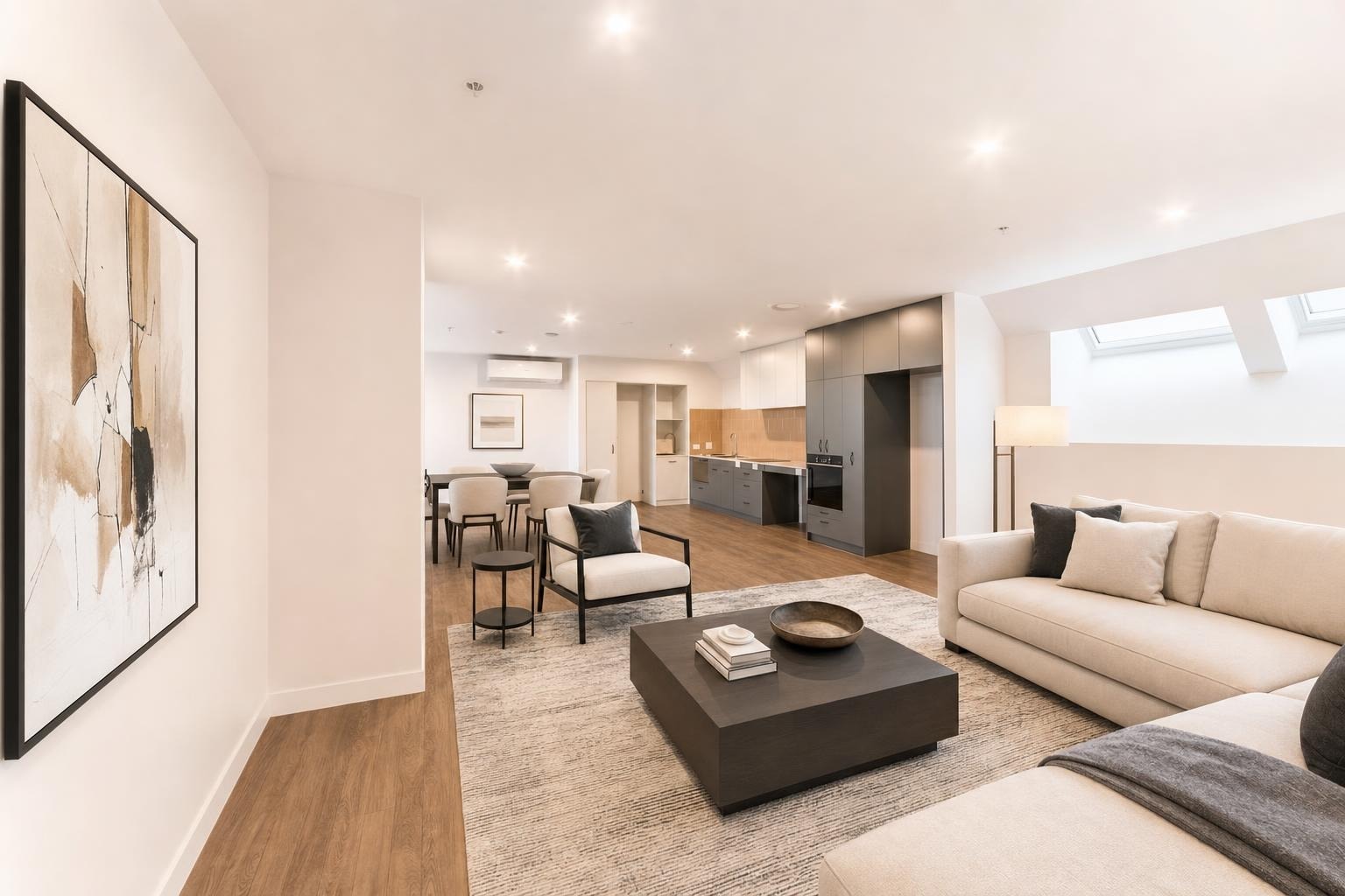 Modern living room with beige sofas, black square coffee table, single armchair, and abstract wall art.