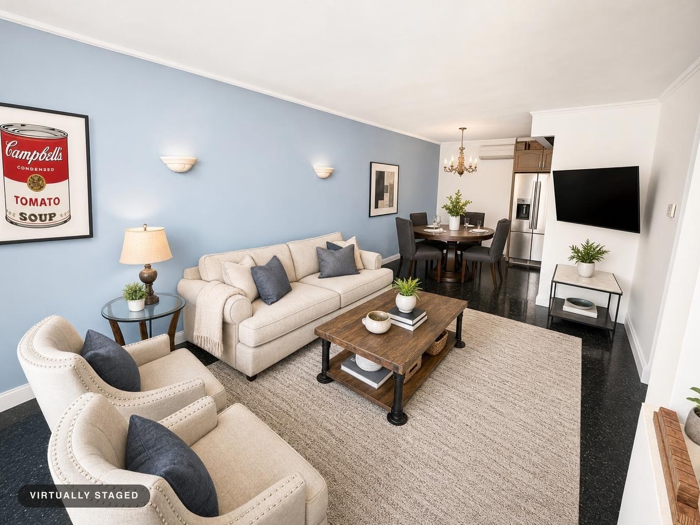 Living room with beige sofa and armchairs, blue accent wall, wooden coffee table, side table with lamp, and dining table in background.