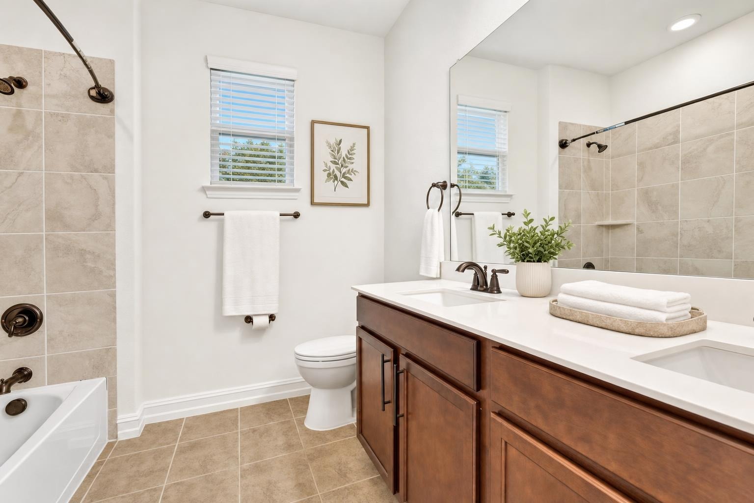 Modern bathroom with beige floor tiles, dark wood vanity with two sinks, white towels, and a tiled bathtub with bronze fixtures.