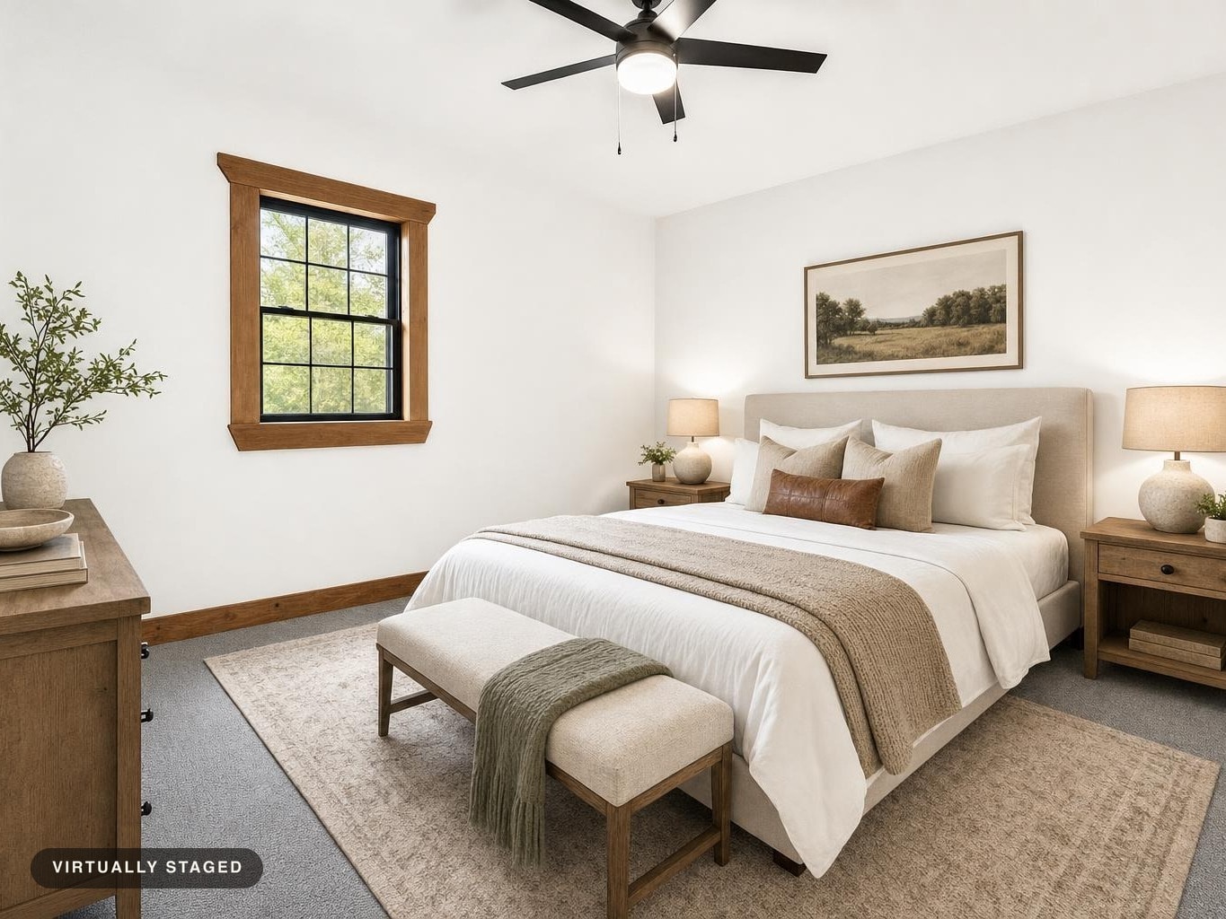 Bedroom with beige upholstered bed, wooden nightstands, lamps, window with wood trim, and bench at foot of bed.