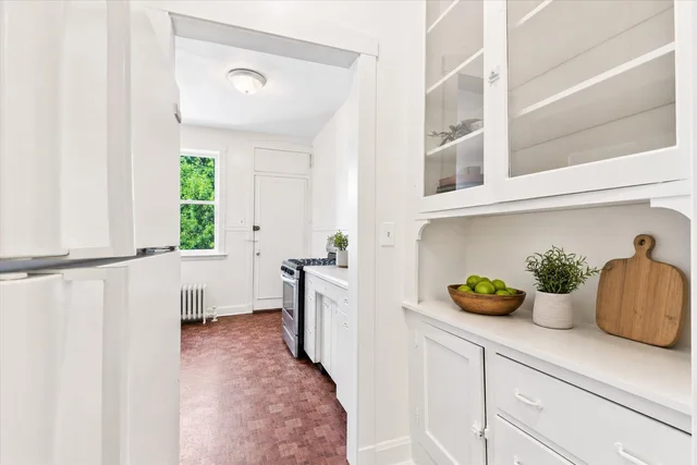 White kitchen with white cabinets, wood parquet floor, stove and window showing greenery outside.