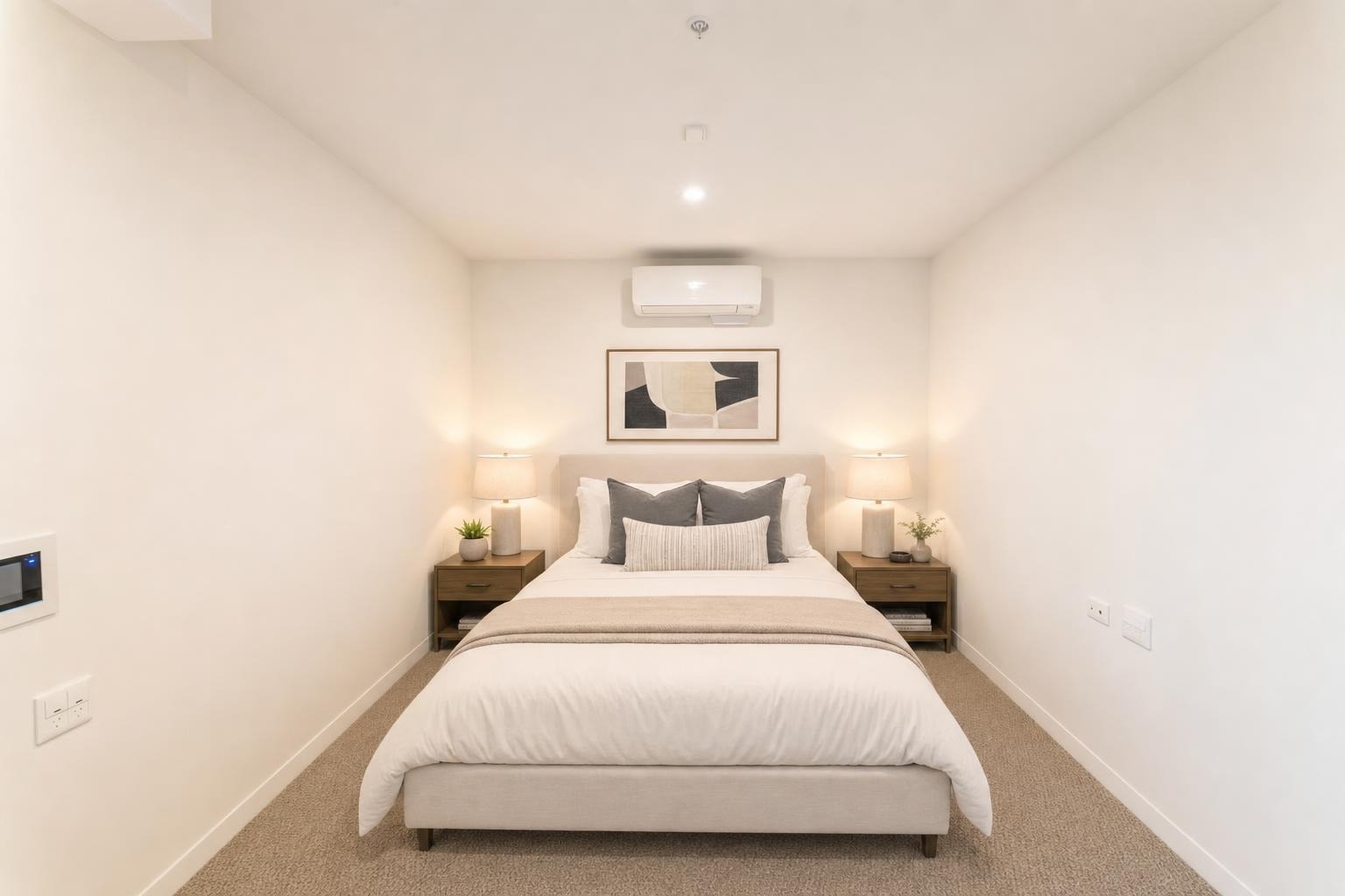 Minimalist bedroom with a bed centered between two matching nightstands with lamps and an abstract art piece above the bed.