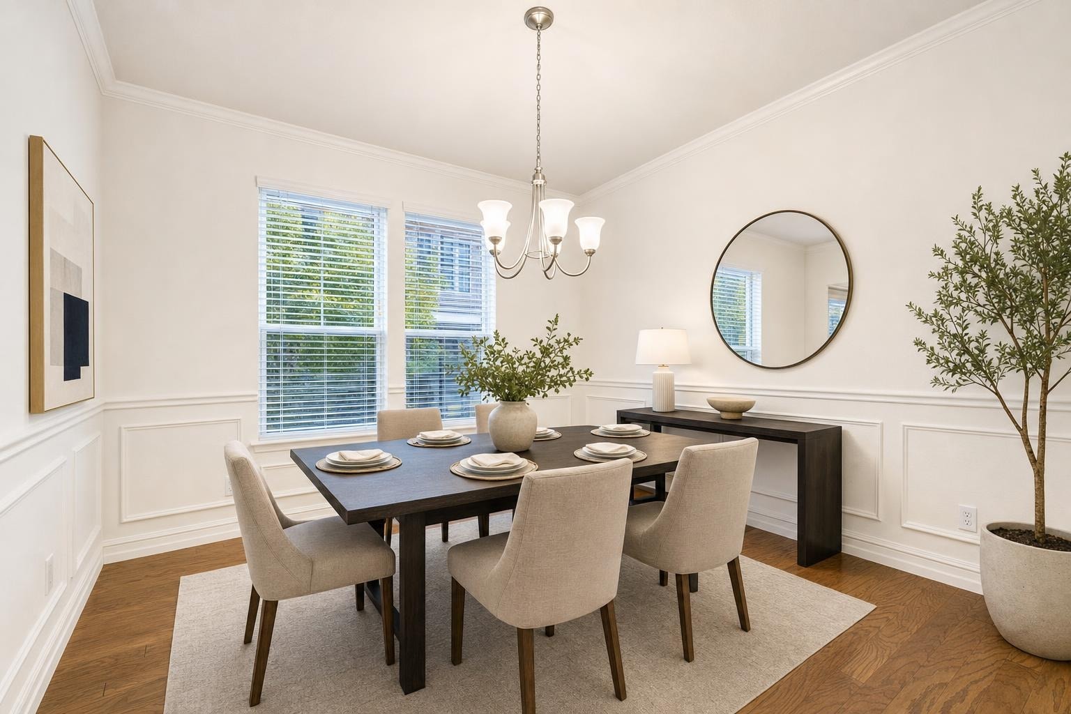 Modern dining room with rectangular dark wood table, six beige upholstered chairs, large round mirror on wall, and green plant in corner.