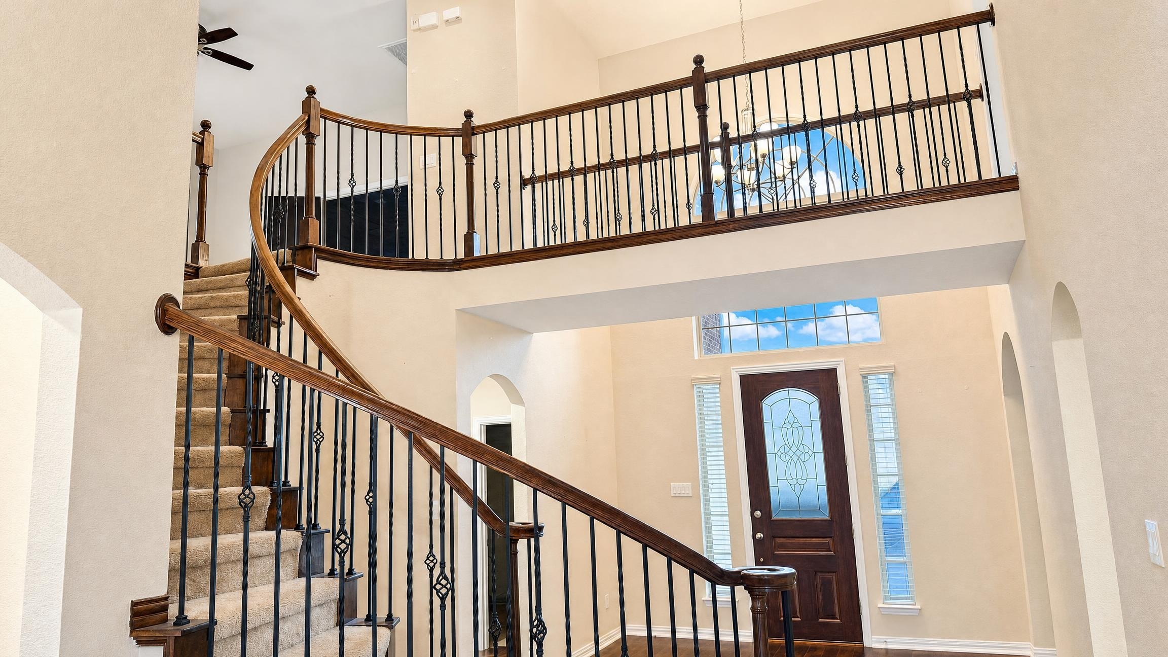 Bright entryway with a curved wooden staircase having black iron balusters and beige carpet, a wooden and glass front door, and cream walls.