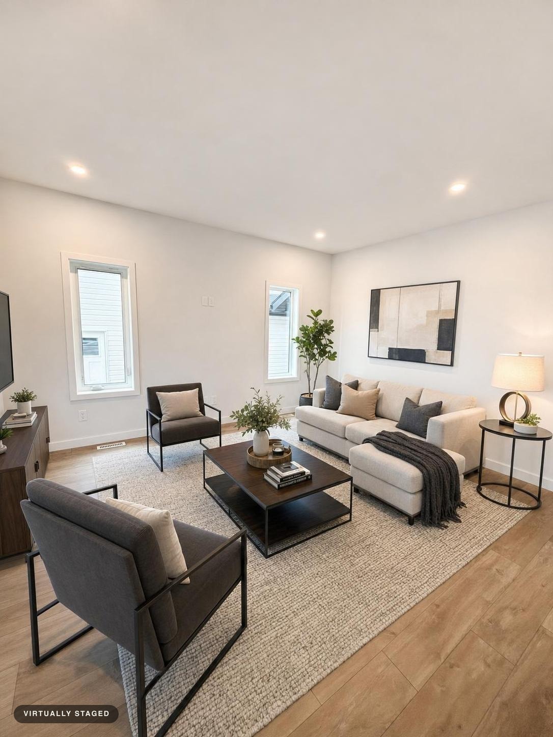 Modern living room with cream sofa, dark armchairs, rectangular black coffee table, neutral rug, side table with lamp, and abstract wall art.