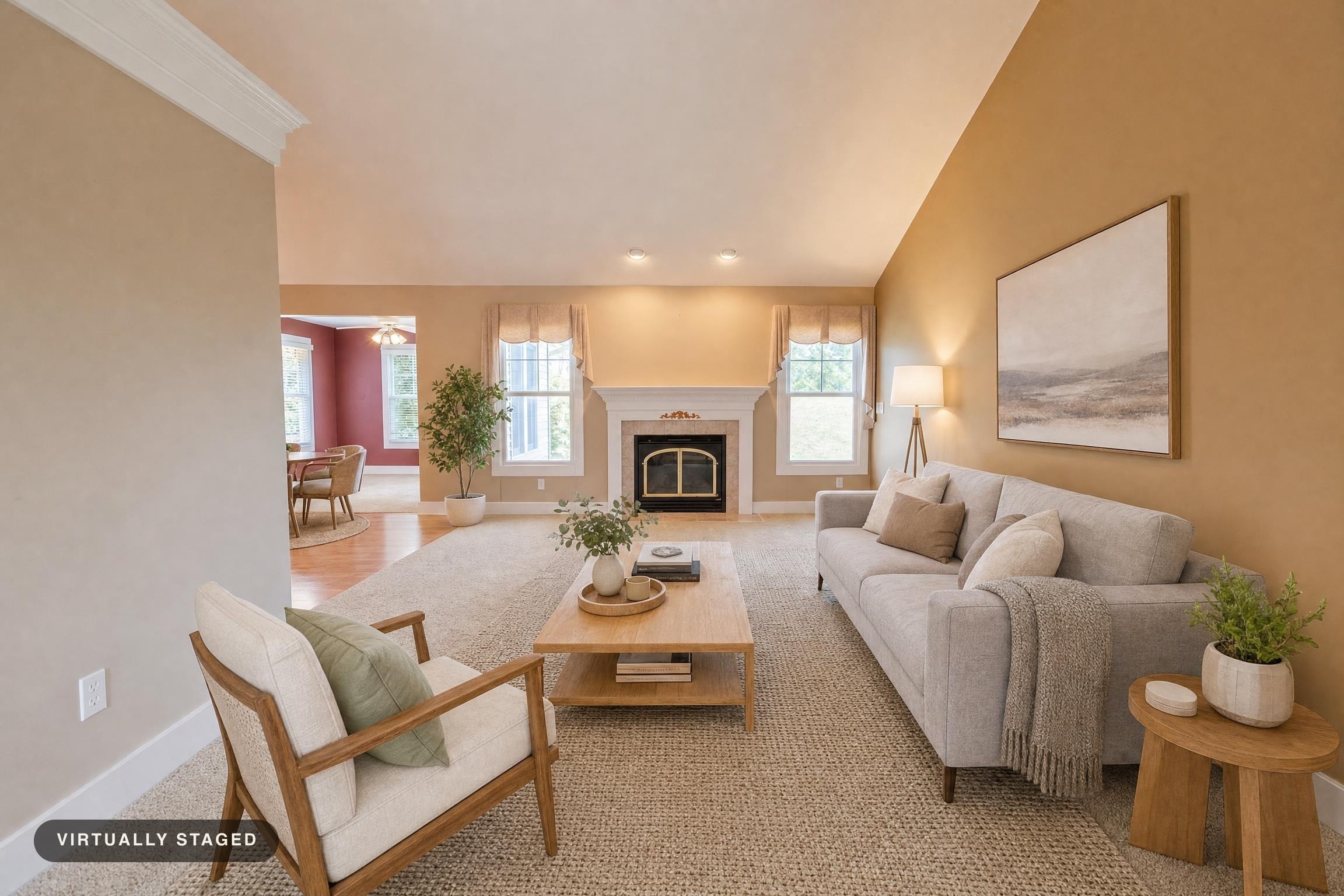 Living room with beige walls, a gray sofa, wooden armchair, coffee and side tables, and a fireplace between two windows.