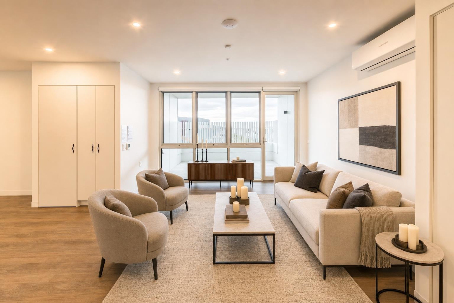Living room with beige sofa and chairs, wooden coffee table, side table with candles, and abstract artwork on a white wall.