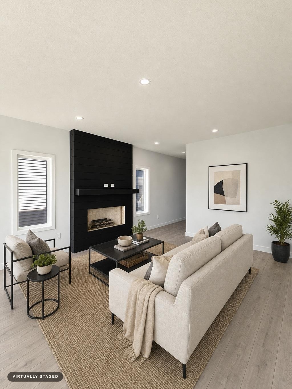Modern living room with beige sofa, black frame armchair, black fireplace wall, light wood floor, and abstract wall art.