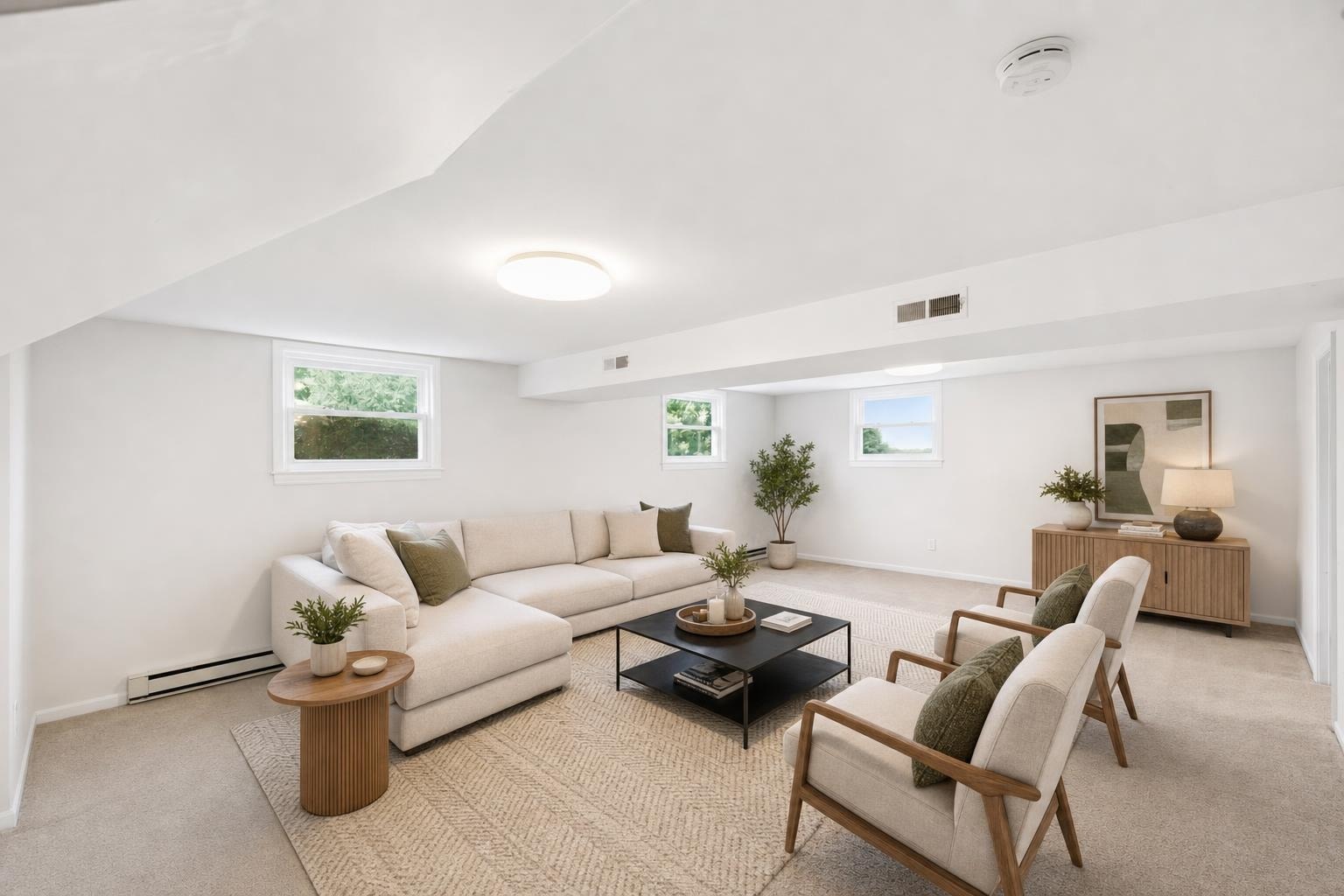 Bright living room with beige sectional, two wood accent chairs with cushions, small plants, and minimal modern decor.