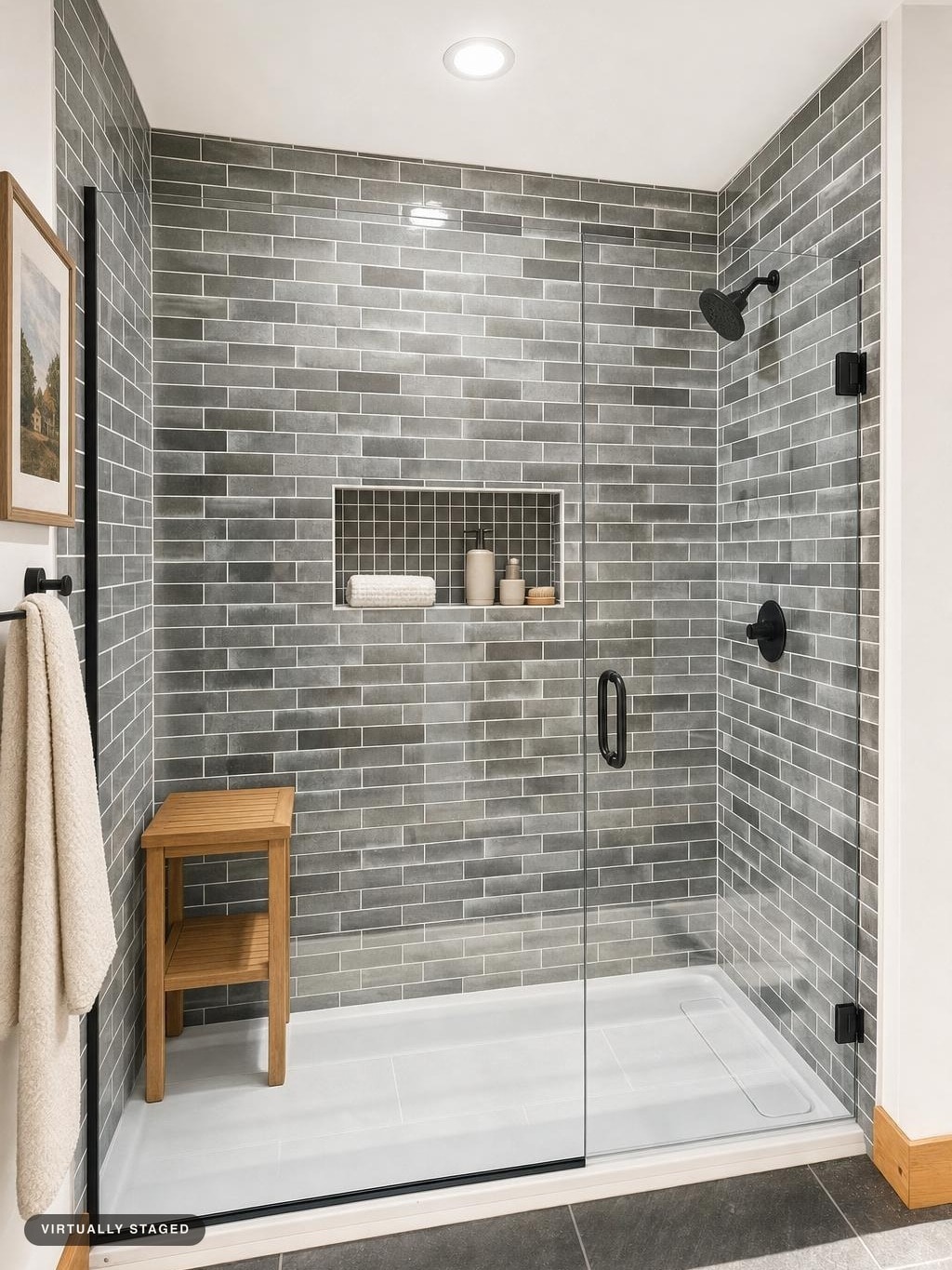 Glass door shower with gray subway tiles, black shower fixtures, wooden bench, and built-in niche with bath items.