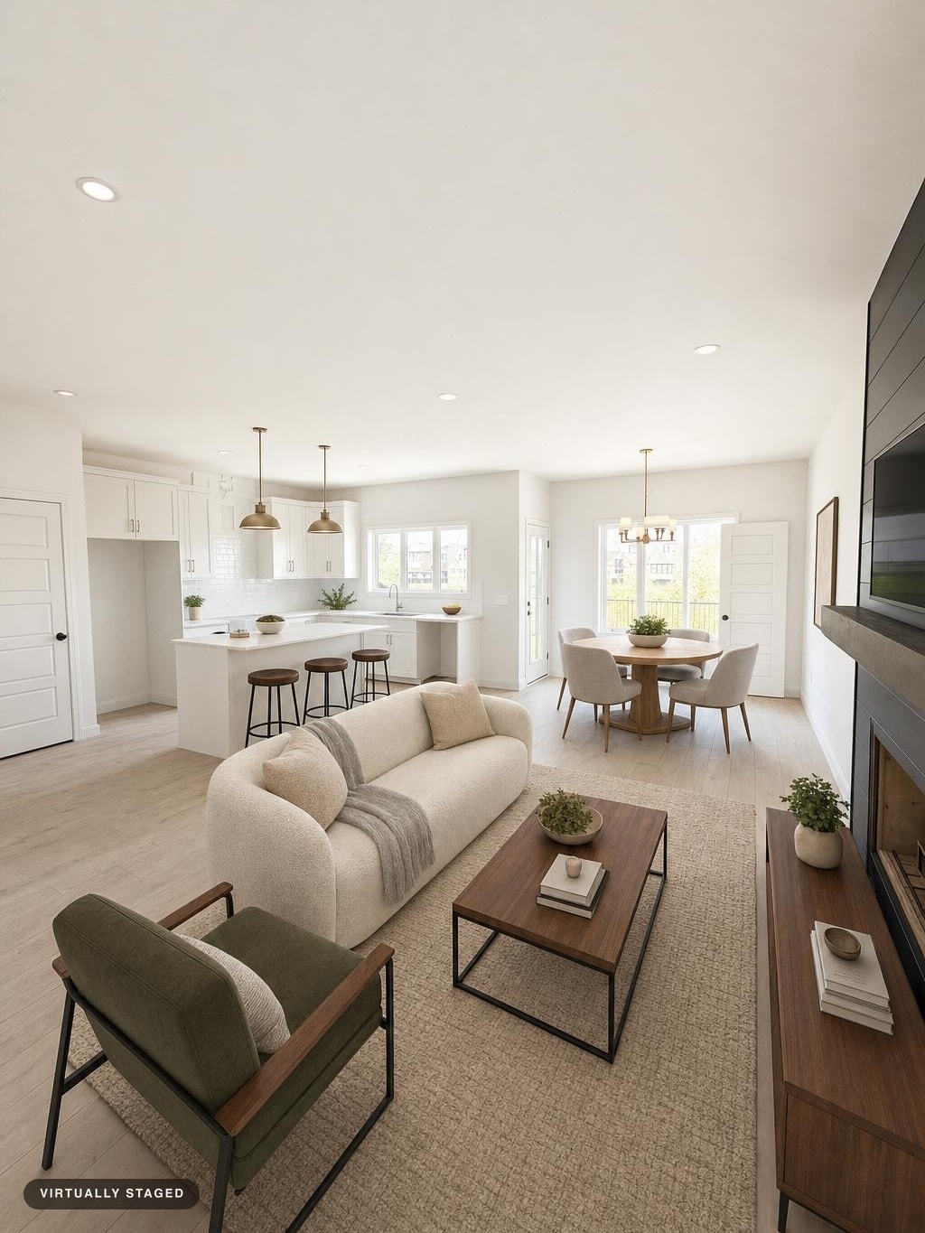 Modern living room with cream curved sofa, green armchair, wood coffee table, and light-filled kitchen and dining area in background.