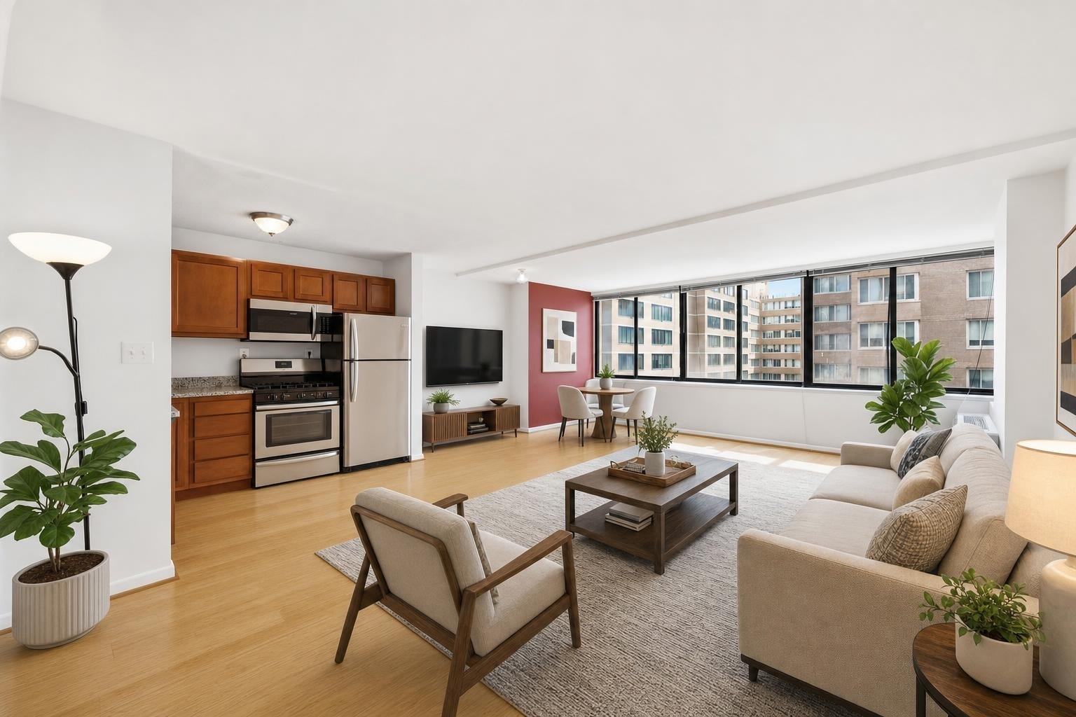Living room with beige sofa, wood-framed armchair, wooden coffee table, floor lamp, and kitchen area with stainless appliances.