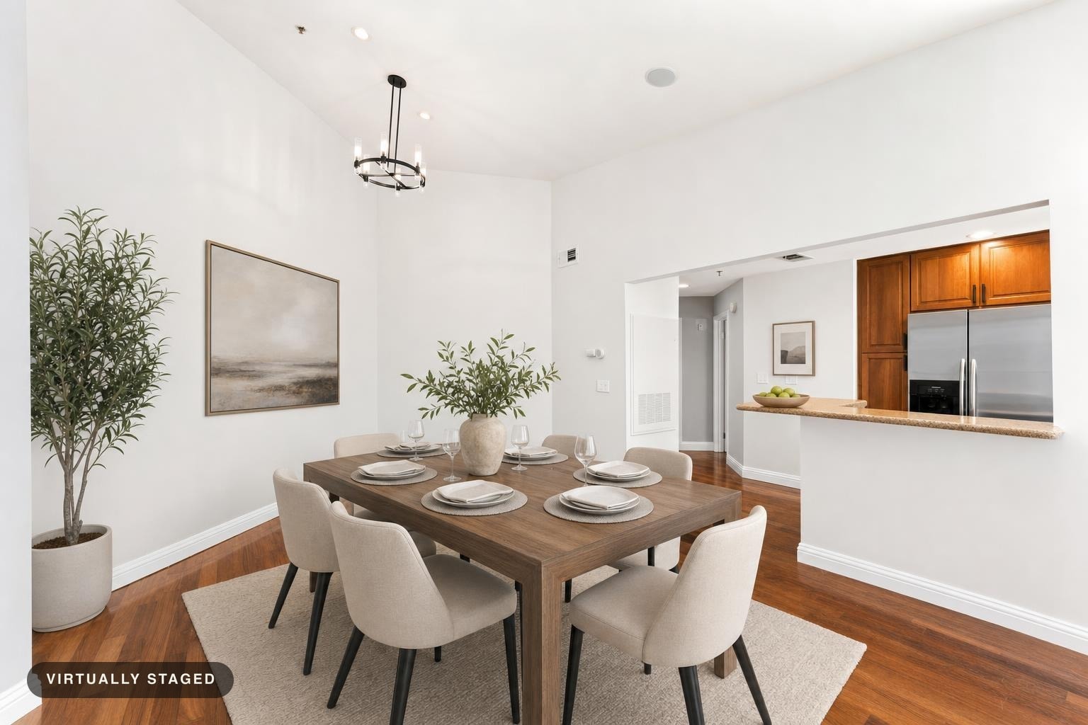Modern dining room with wooden table set for six, beige upholstered chairs, white walls, and greenery in vases and pots.