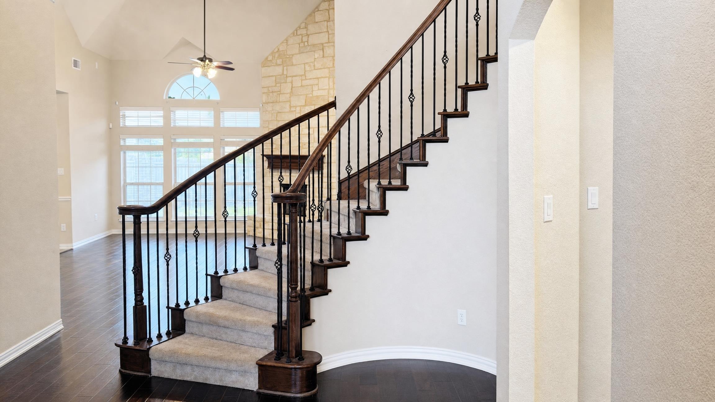 curved staircase with dark wood handrails and iron balusters in a bright entryway with beige walls and dark hardwood floors