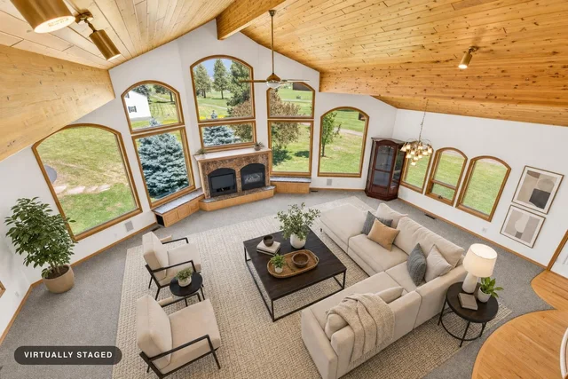 Living room with vaulted wood ceiling, large arched windows, beige sectional sofa, two armchairs, and a coffee table.