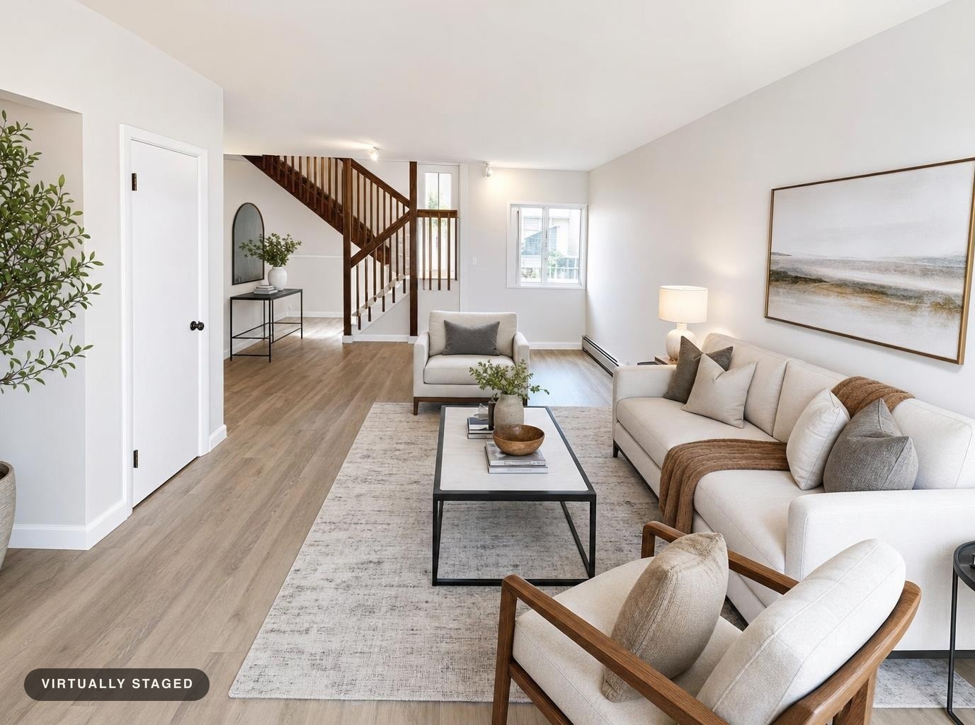 Bright modern living room with beige sofa, armchairs, black metal coffee table, wood staircase, and neutral rug on light wood floor.