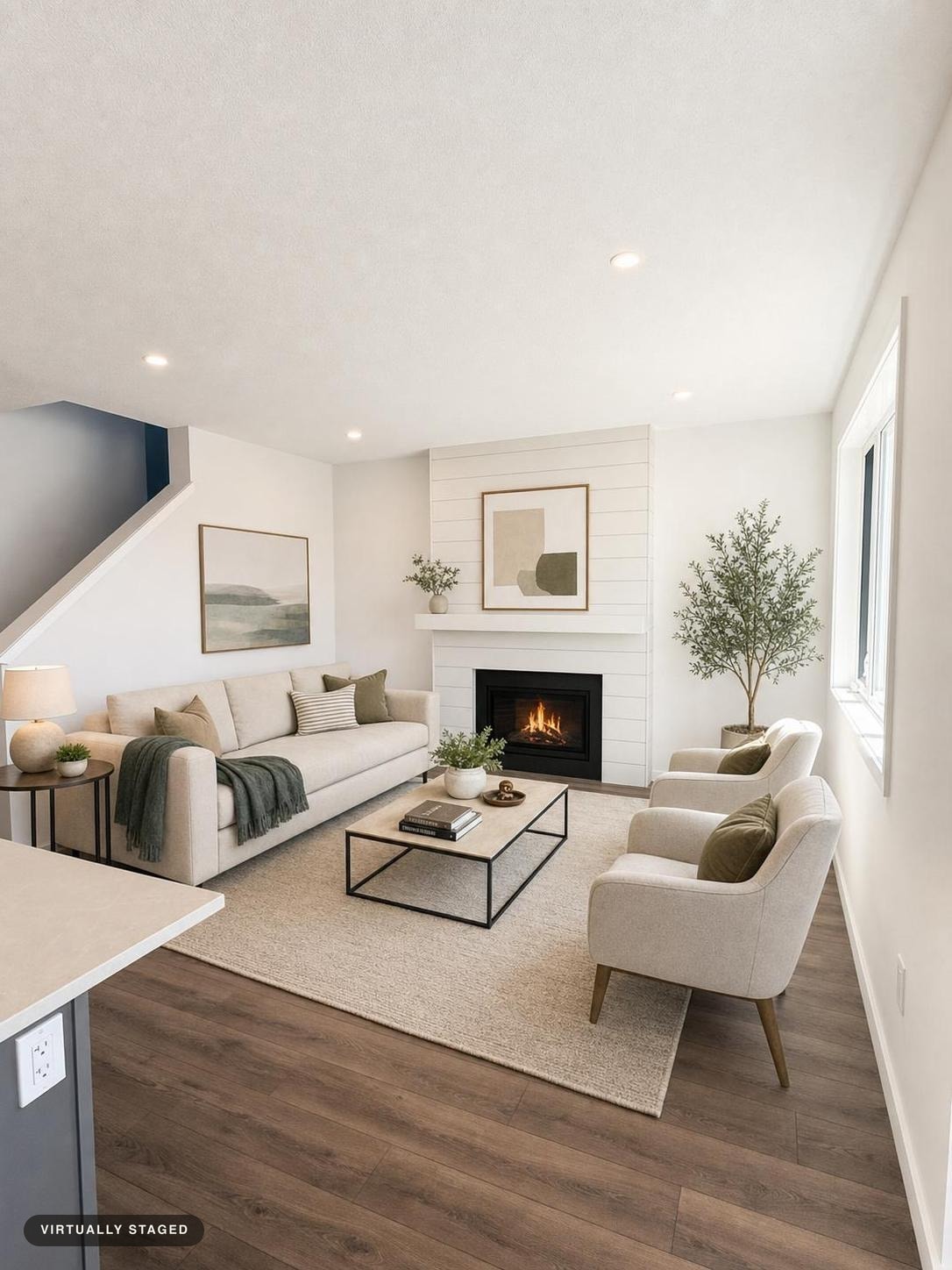 Modern living room with beige sofa and chairs, a black-framed coffee table, a fireplace, plants, and wooden floor.