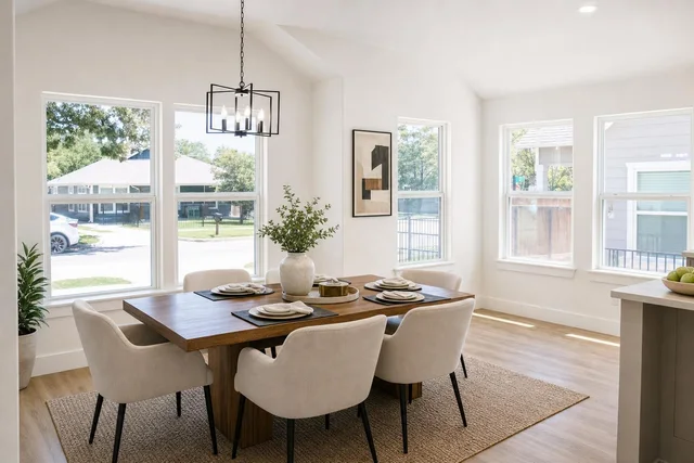 Bright dining room with large wooden table, six beige upholstered chairs, black metal chandelier, and large windows.