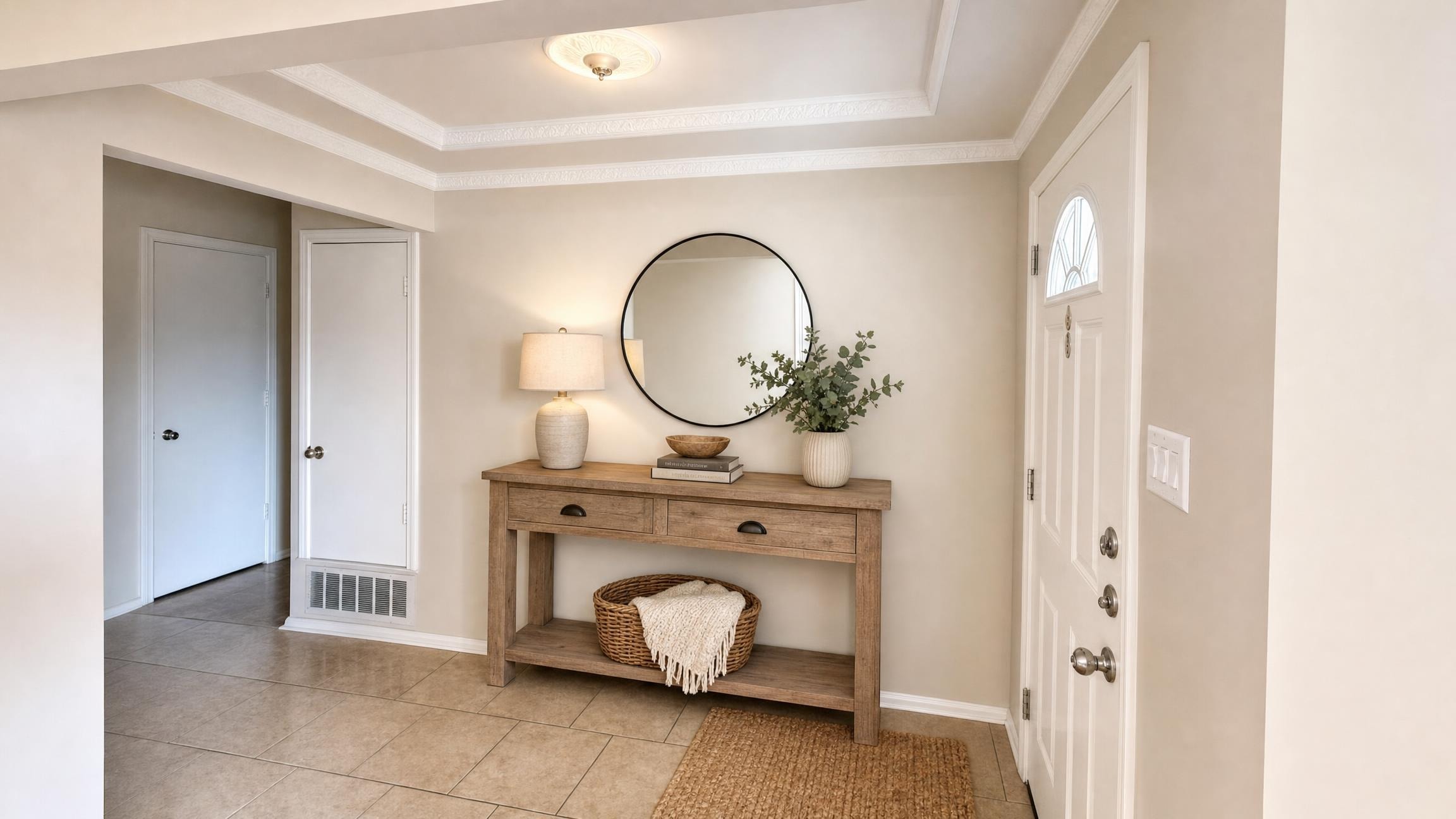 Entryway with beige tile floor, rustic wood console table with round mirror, lamp, woven basket, and white paneled front door.