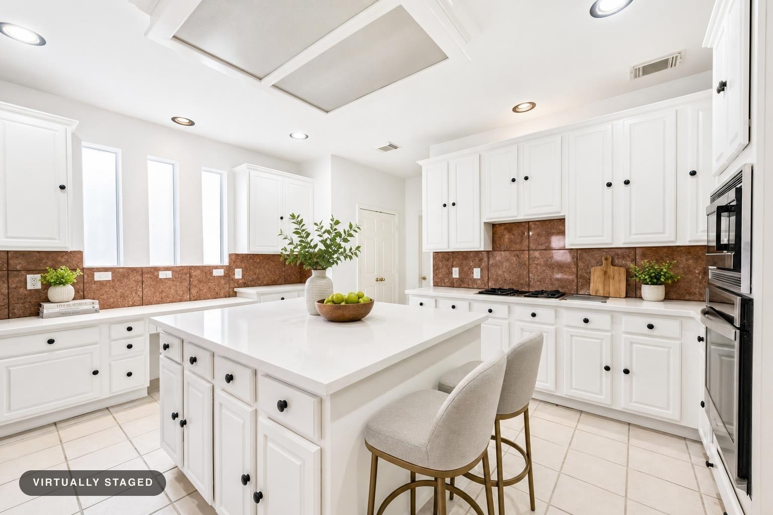 Modern kitchen with white cabinets, large white island, two gray upholstered stools, and brown tile backsplash.