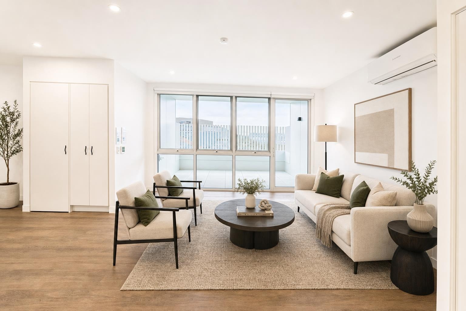 Bright modern living room with cream sofa, two cream and black metal armchairs, round dark wood coffee table, and minimalist decor on beige rug.